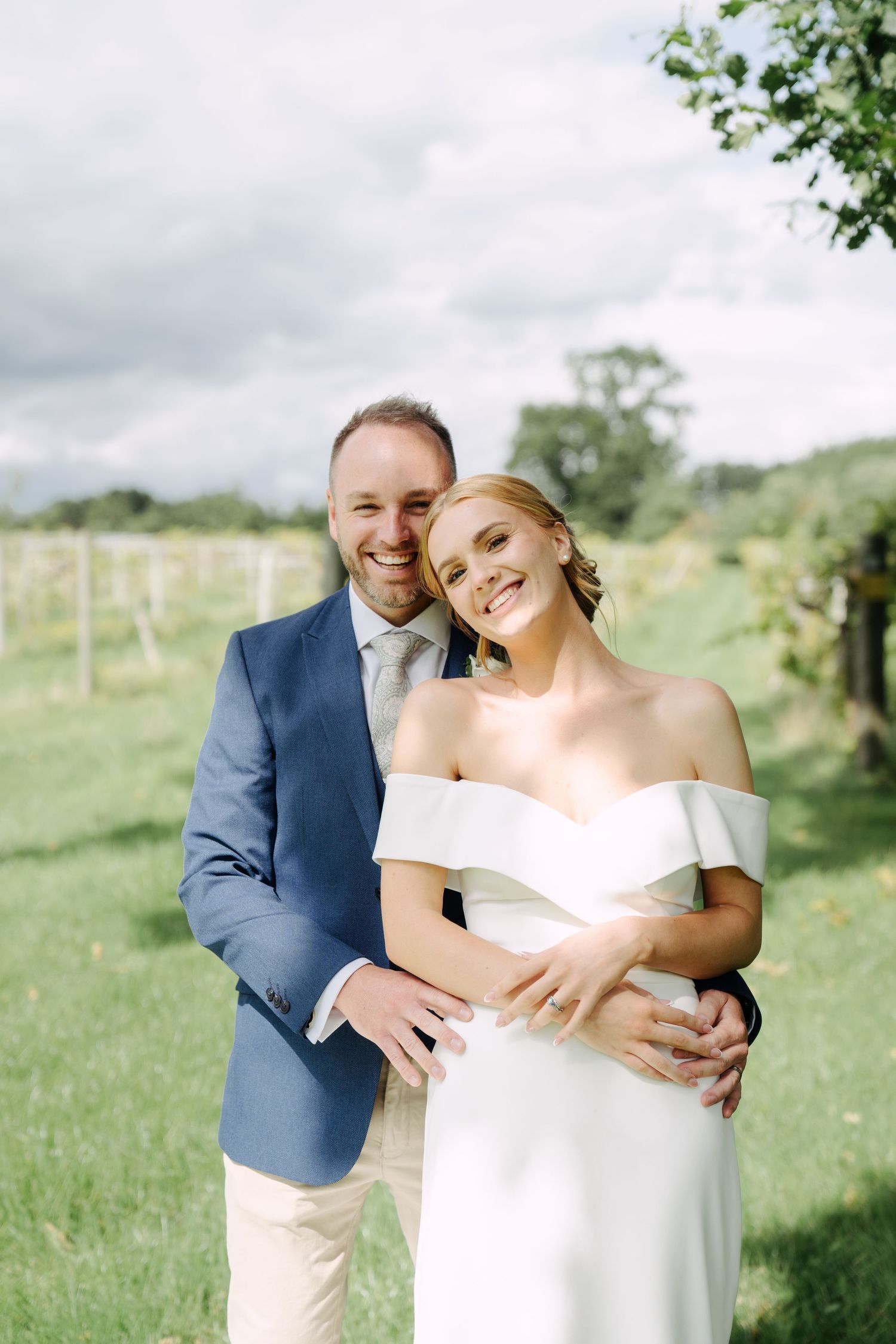 A candid portrait of a bride and groom sharing a quiet moment together beneath leafy trees, captured in soft natural light.