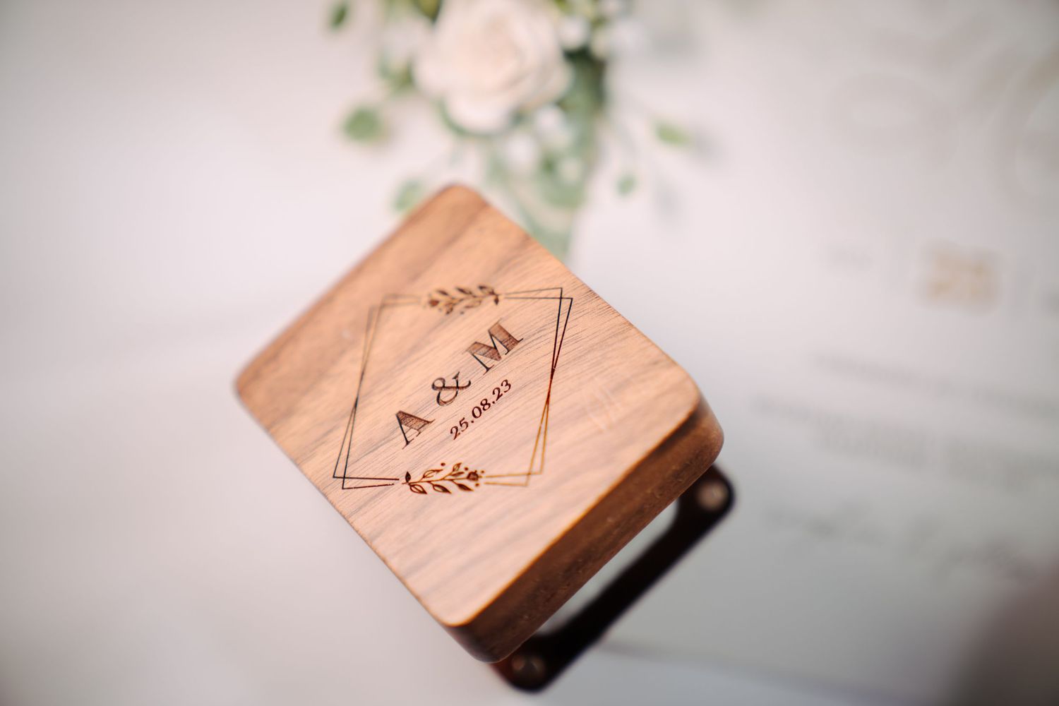 Custom engraved wooden ring box with initials and wedding date, styled with soft florals for detail photography.