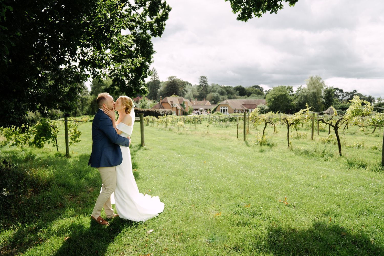 A candid portrait of a bride and groom sharing a quiet moment together beneath leafy trees, captured in soft natural light.