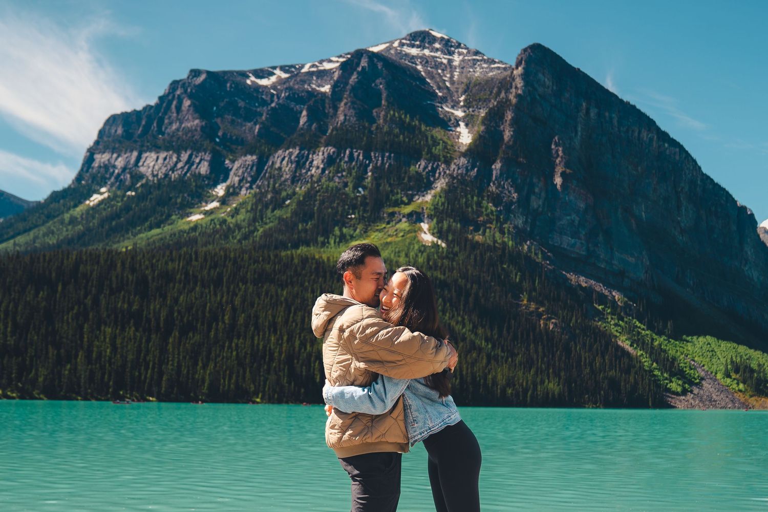 Couple embracing at Lake Louise, with turquoise water and dramatic mountain peaks behind them, capturing a romantic and natural moment.