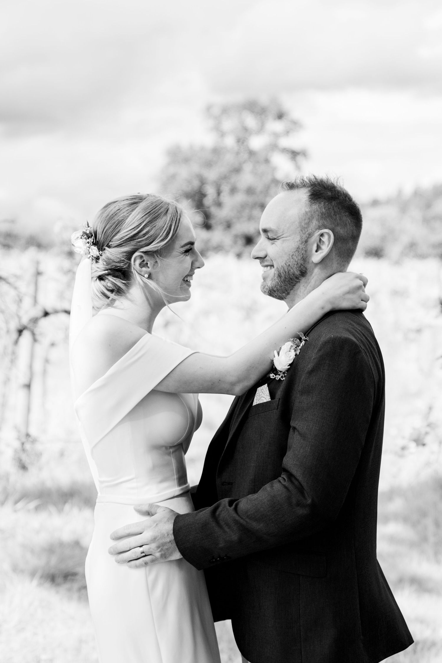An intimate outdoor wedding photograph of a bride and groom laughing together among vineyard rows. black and white image. candid.