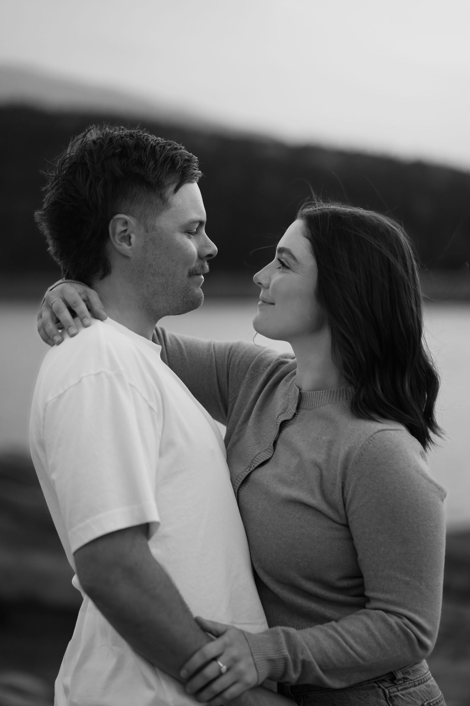 Couple holding each other and looking into each other’s eyes during an engagement session at Lake Minnewanka in Banff, captured in black and