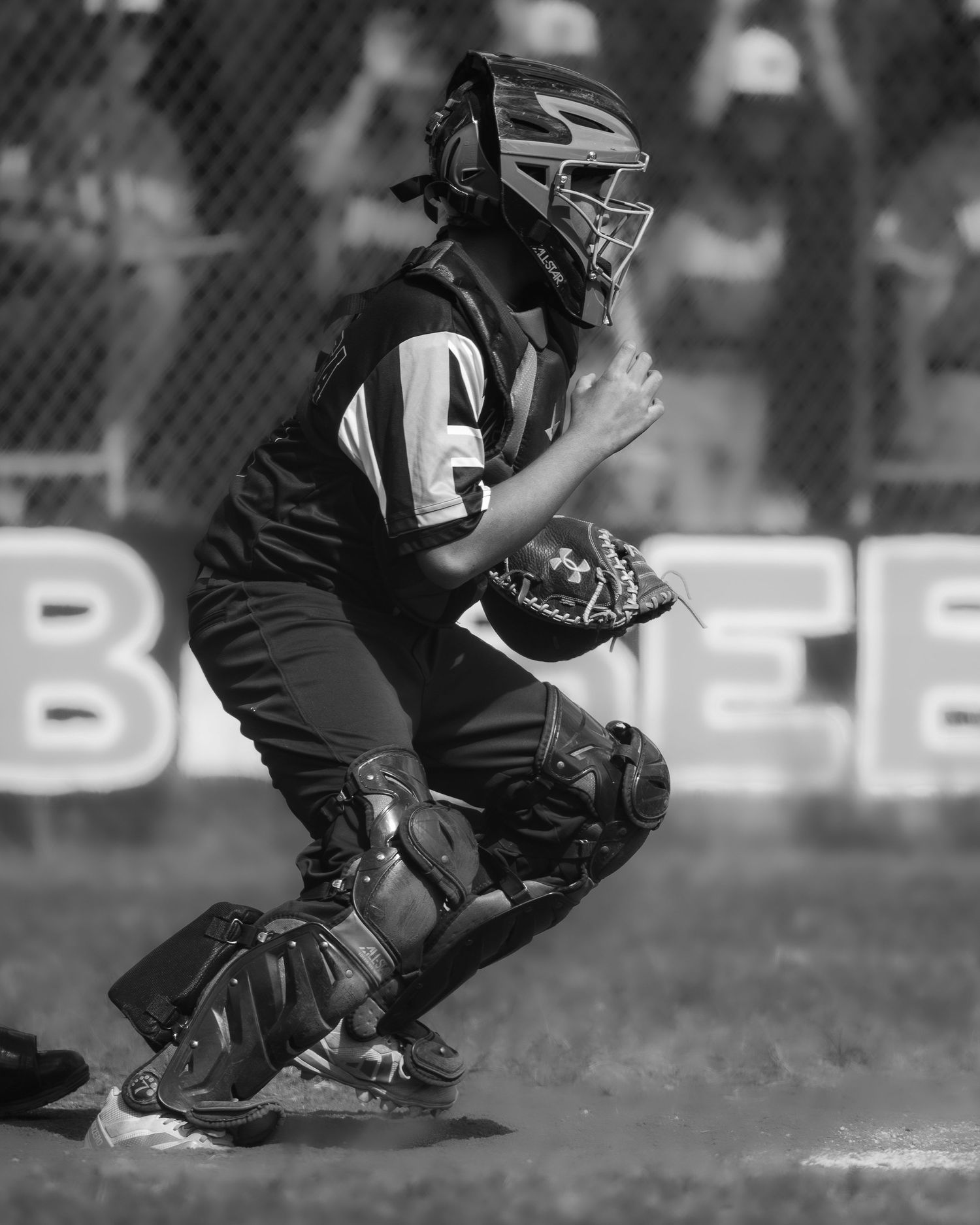 Black and white photo of a youth baseball catcher in full gear crouching in position during a game.