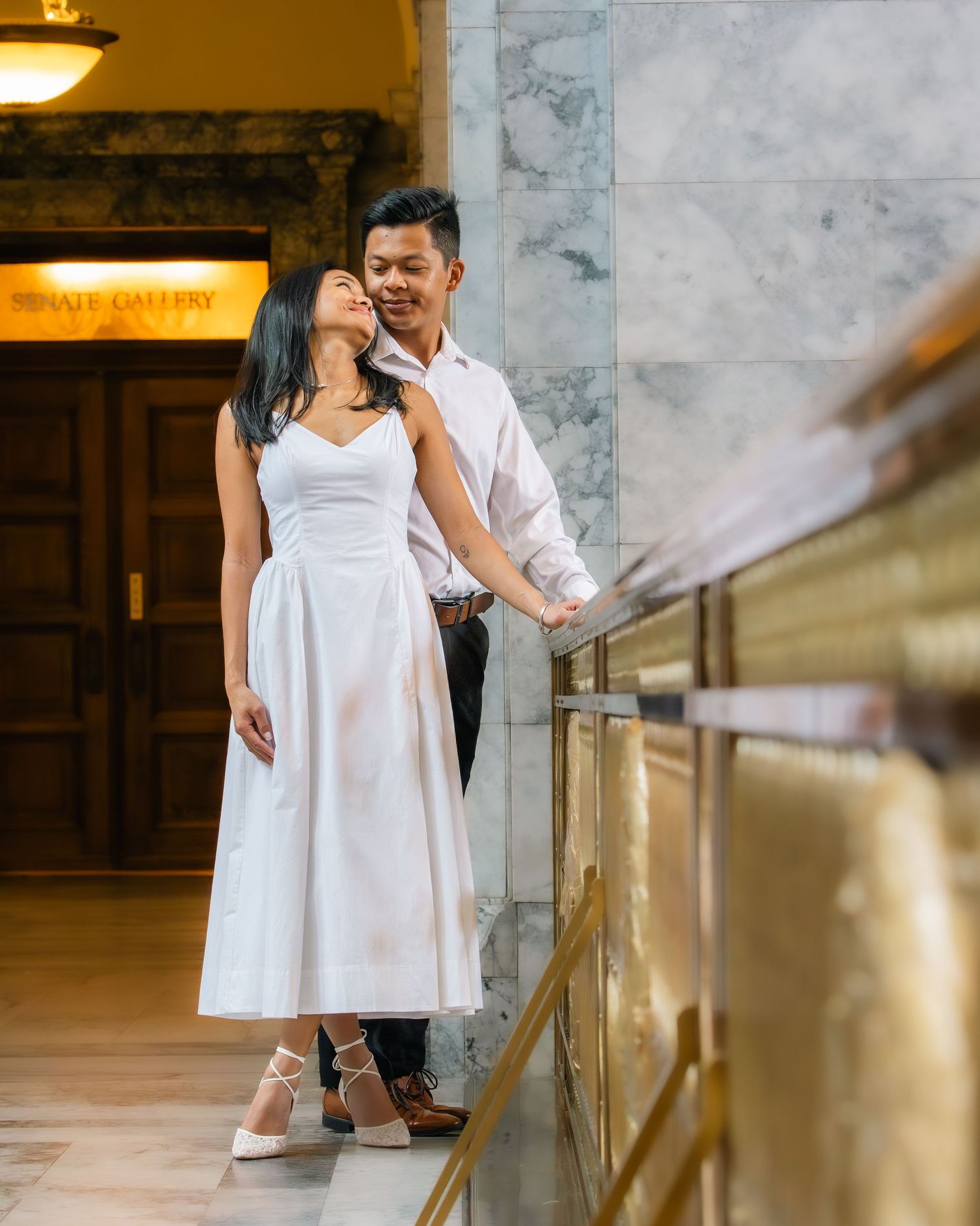 Couple in elegant attire poses on marble staircase near private gallery entrance in romantic engagement photo.