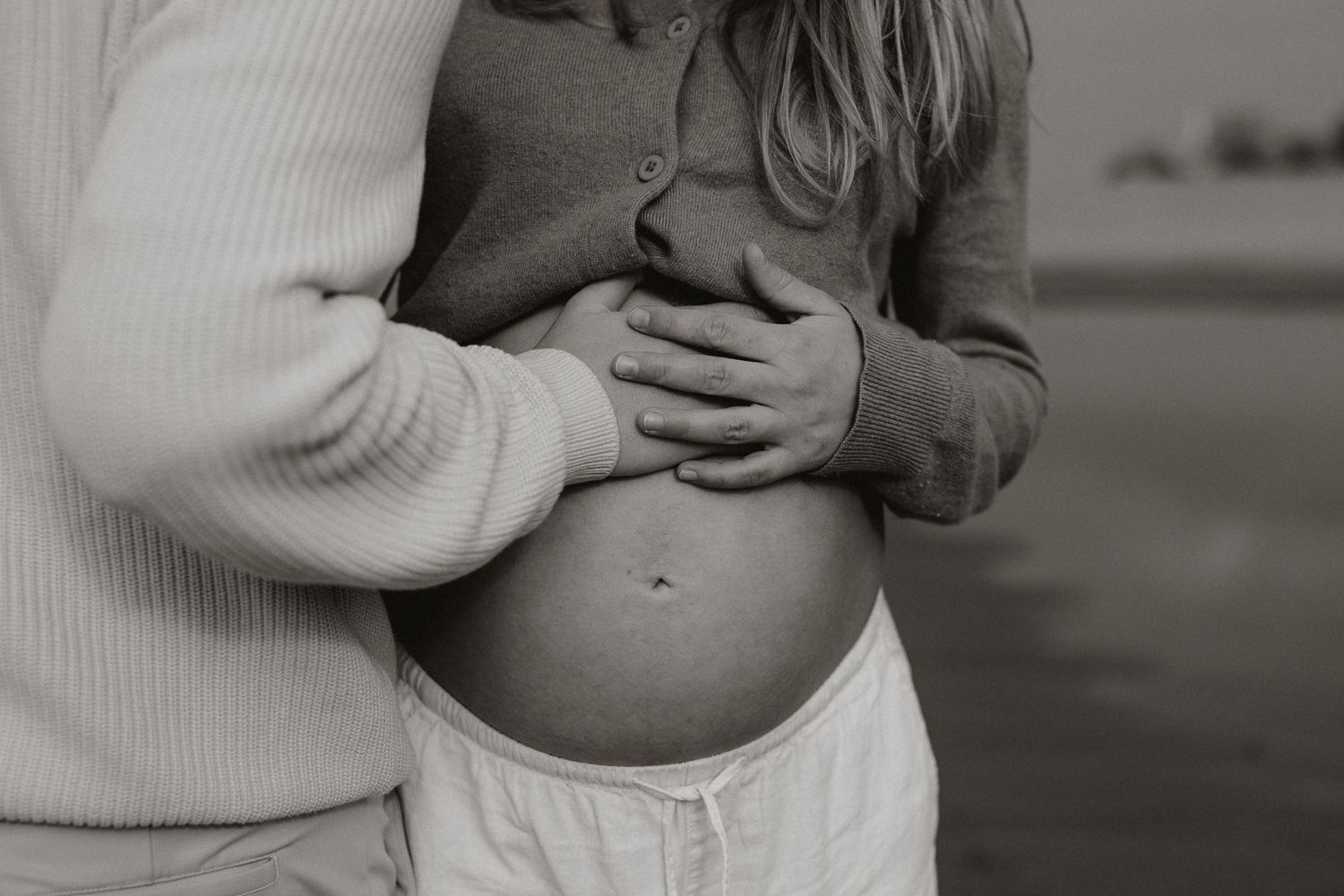 Black and white close-up of couple's hands cradling pregnant belly in maternity portrait.