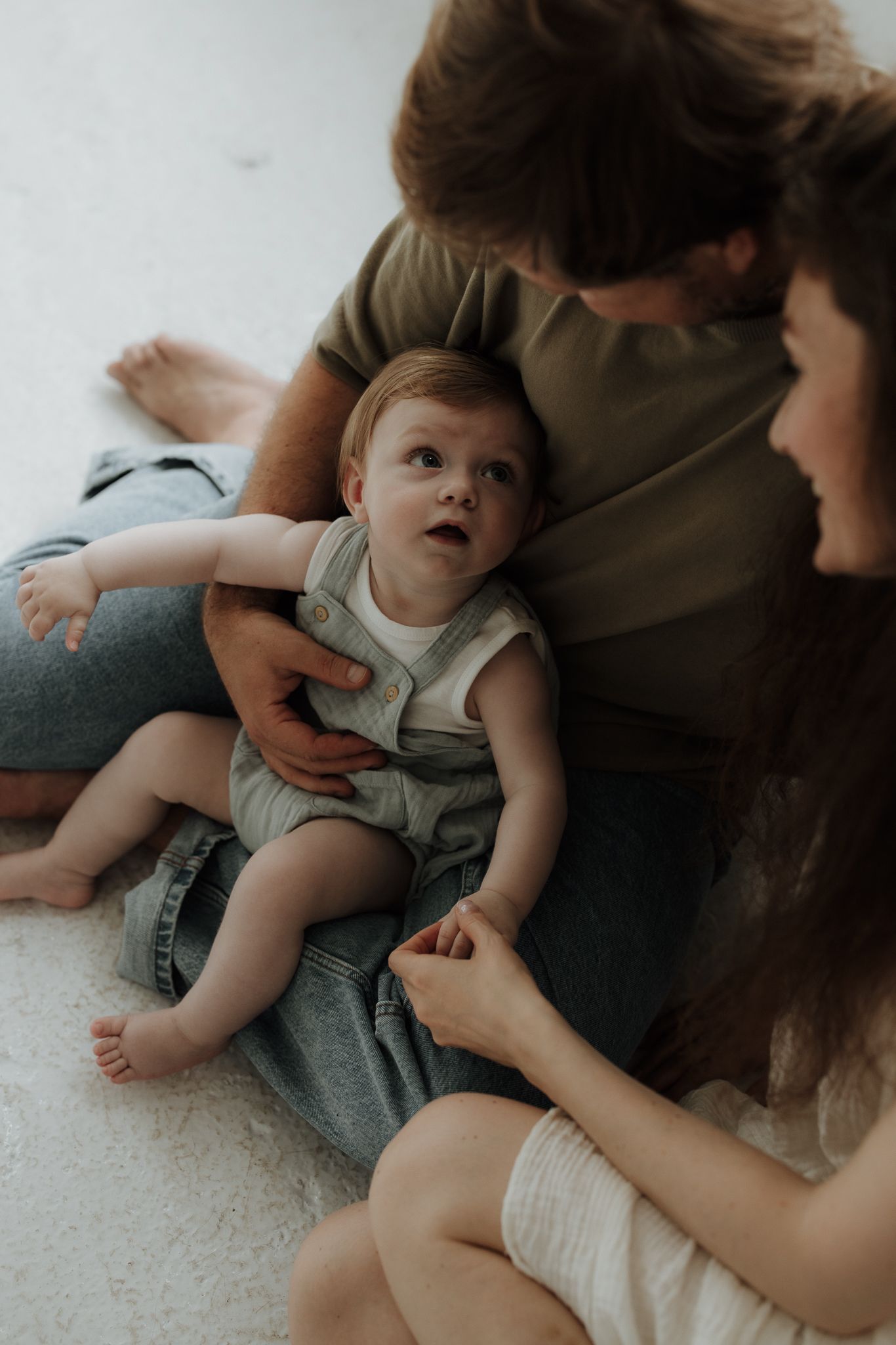 Parents sitting on floor with their baby in a cozy indoor setting, sharing a tender family moment.