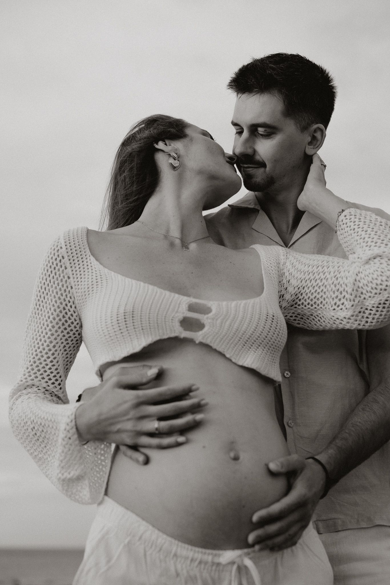 Black and white photo of couple sharing intimate moment, pregnant woman cradling belly with partner.