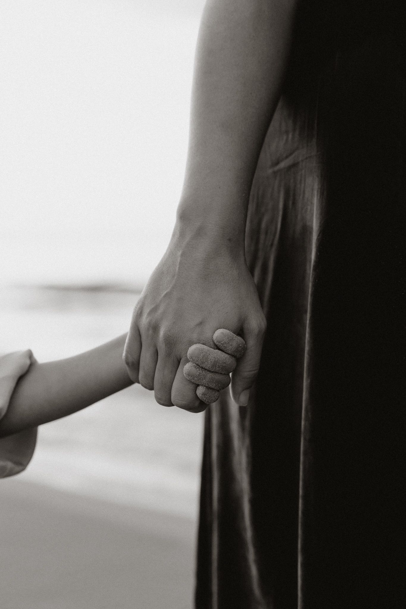 Black and white close-up of an adult holding a small child's hand tenderly.
