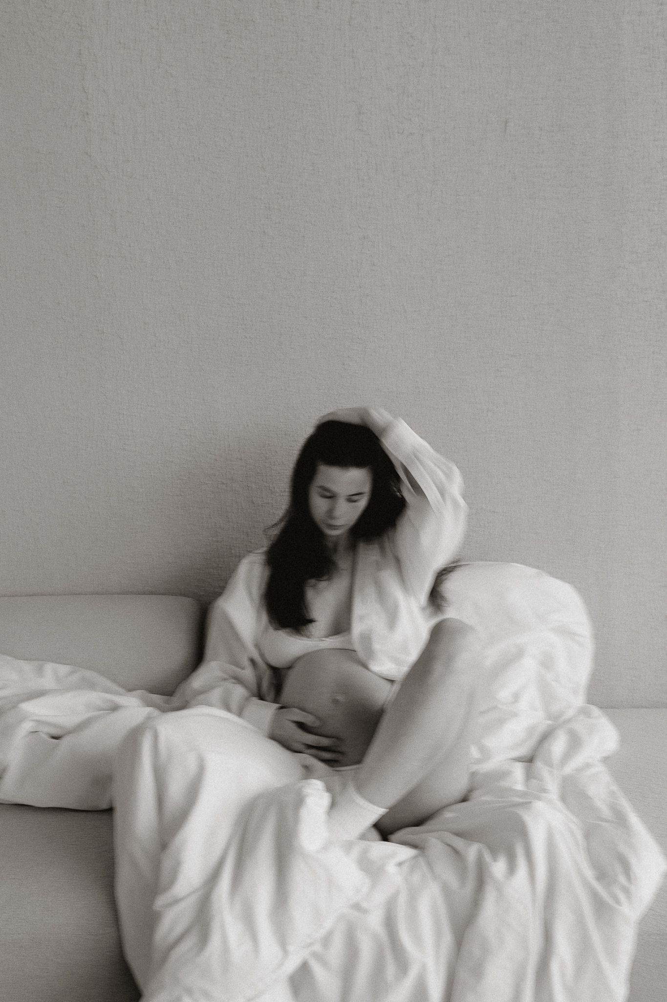 Black and white photo of pregnant woman on couch cradling baby bump with hand in hair.