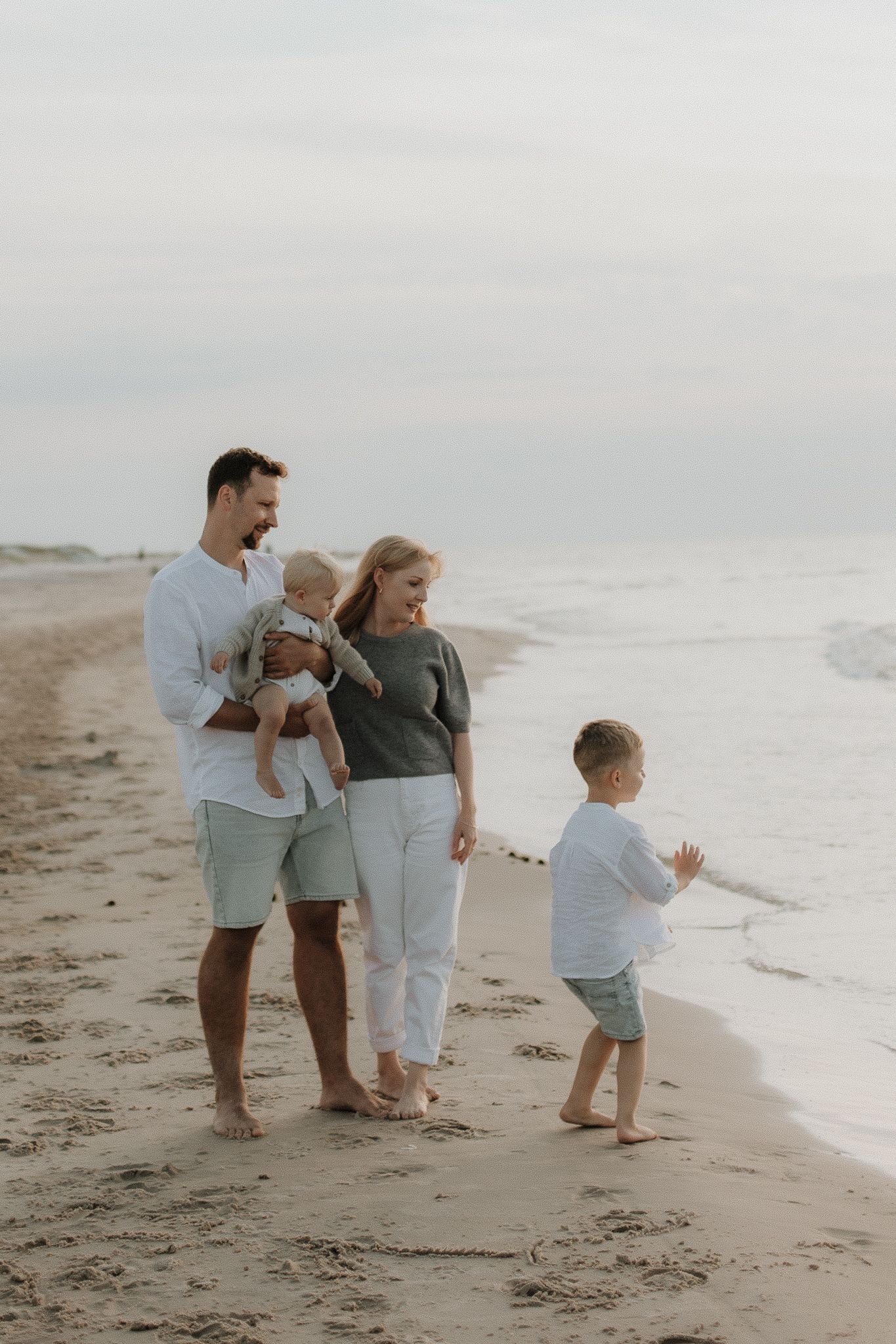 Joyful family with two children walking barefoot on a sandy beach together.