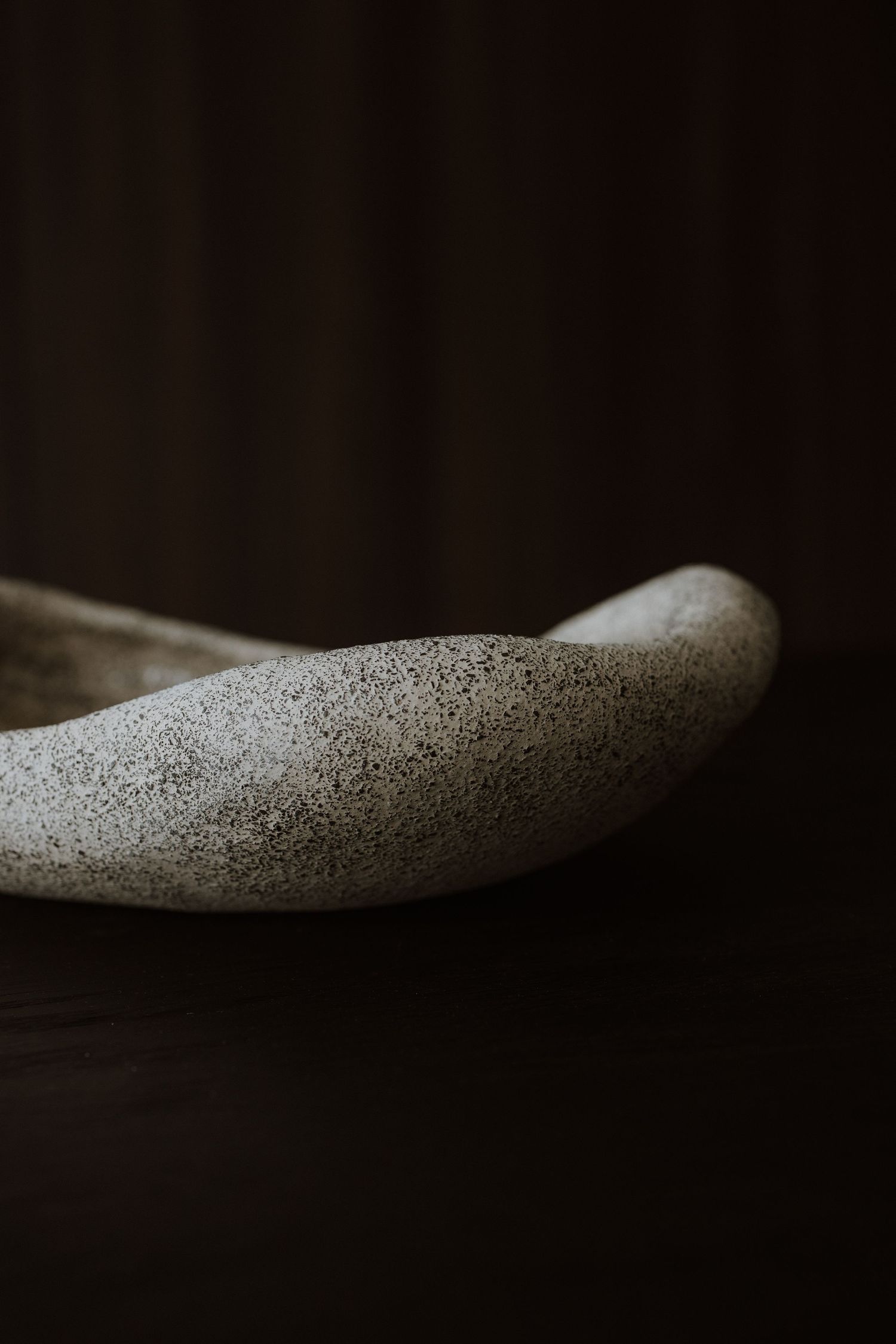 Close-up of a speckled gray ceramic bowl with organic curved edges on a dark wooden surface.