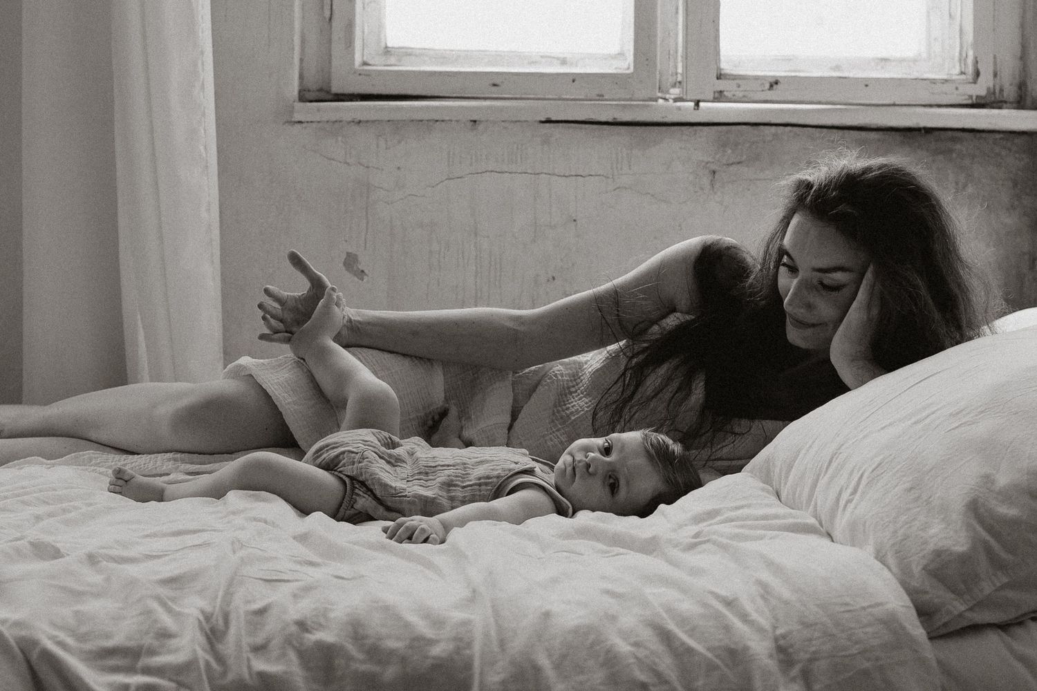 Mother and baby bonding on white bed in intimate black and white lifestyle photography.