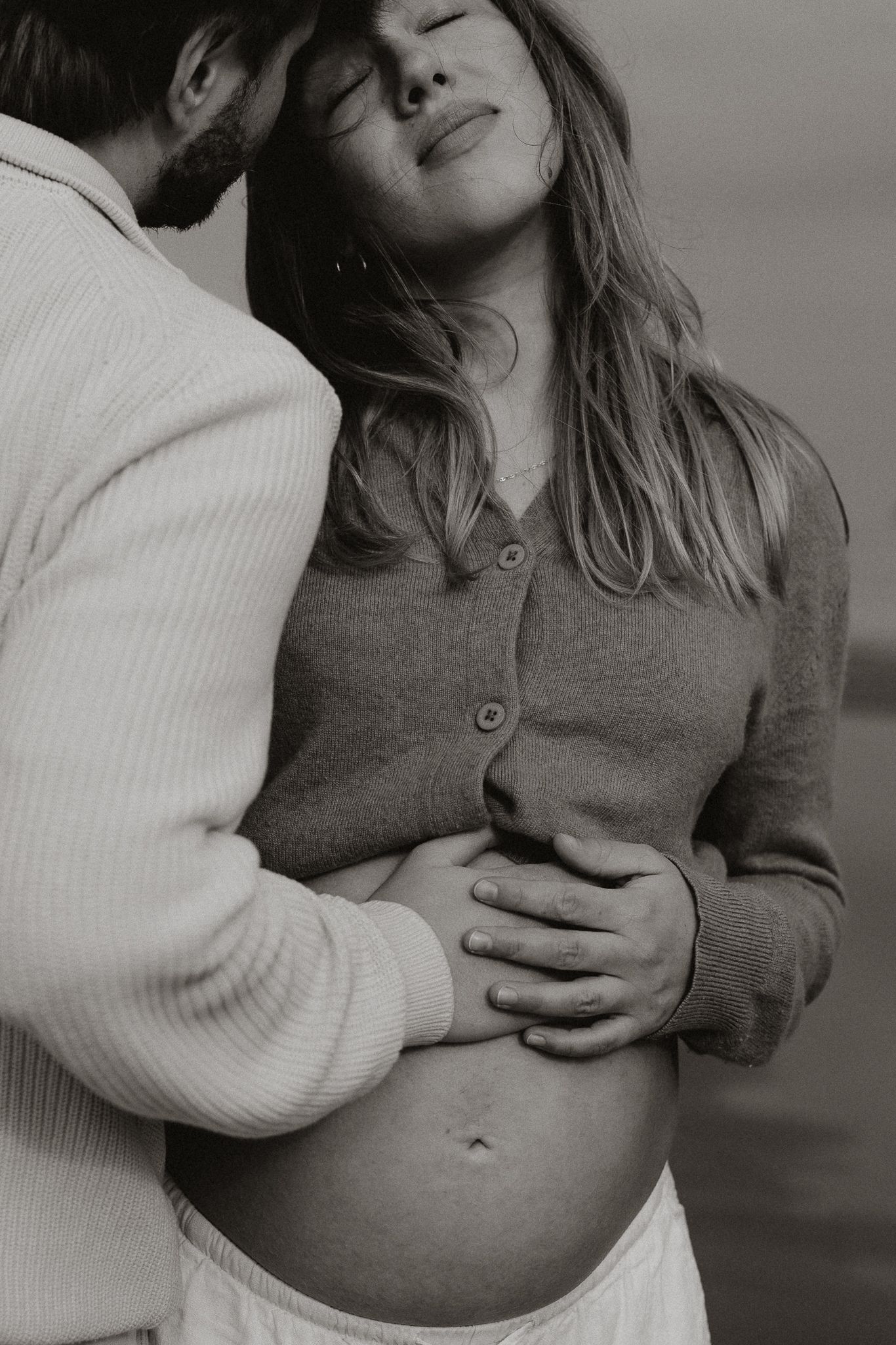 Black and white photo of couple cradling pregnant belly outdoors.