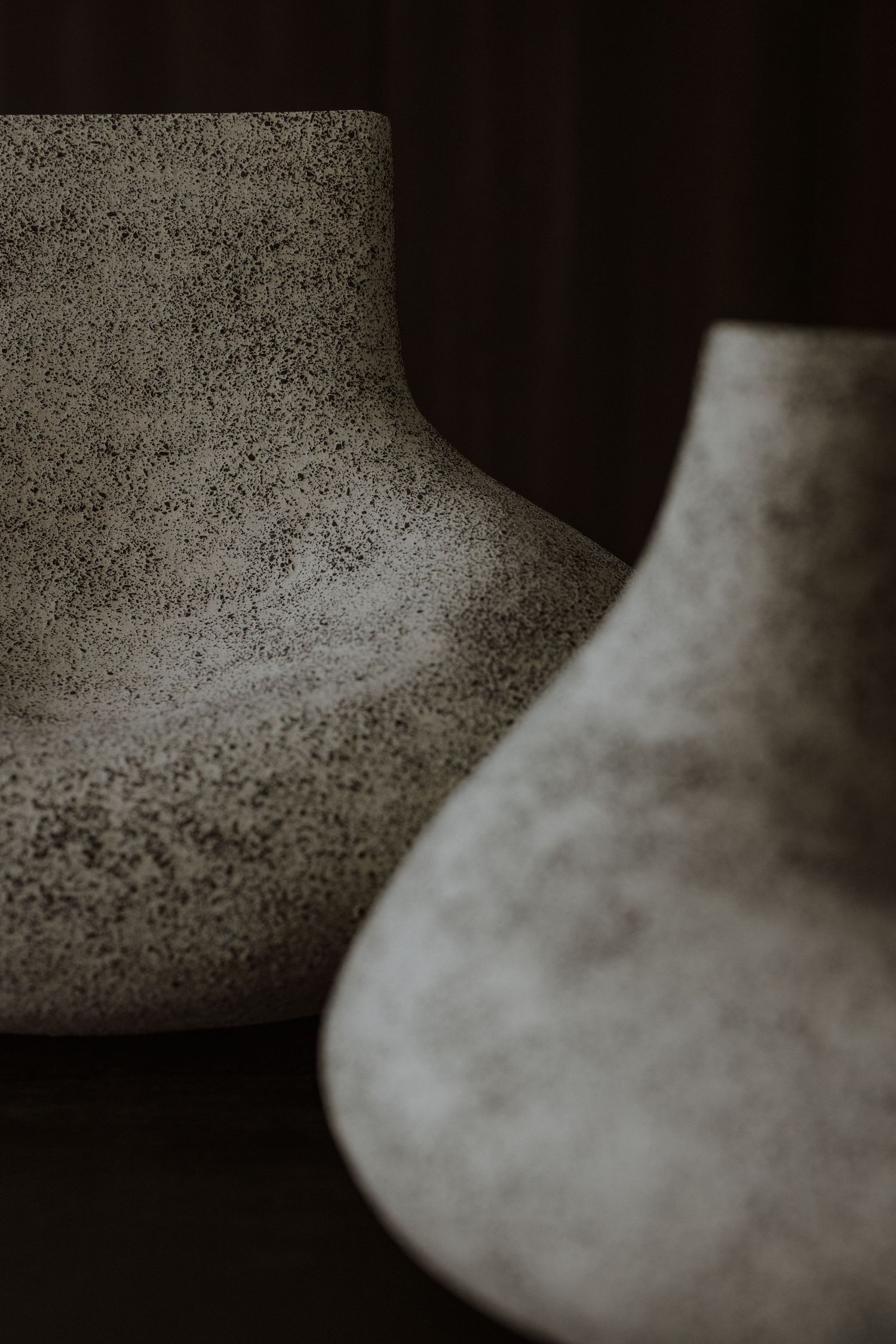 Two matte speckled ceramic vases with organic shapes displayed against a dark background.