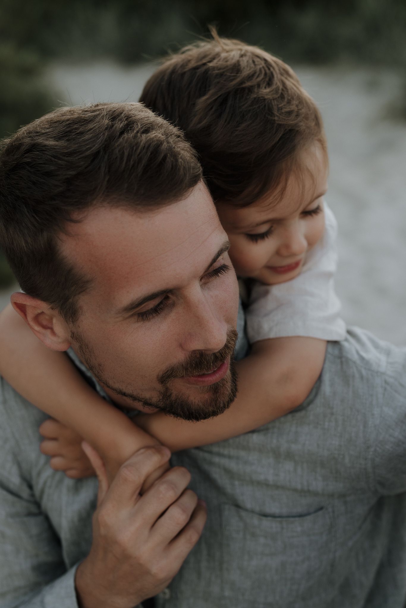 Loving father carrying smiling toddler on his back in a warm outdoor embrace.