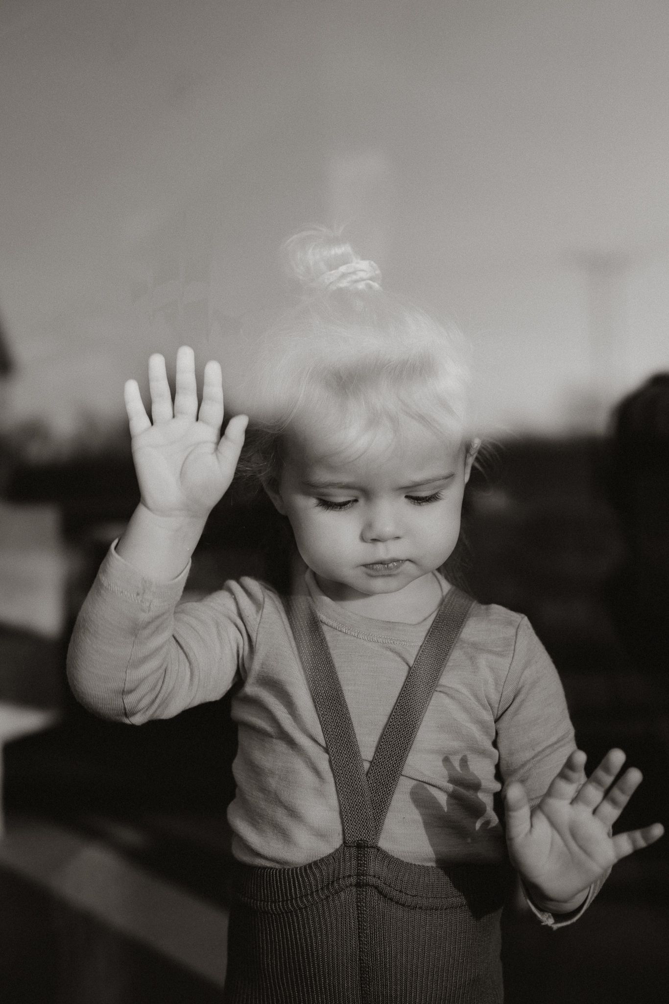 Black and white portrait of a toddler pressing hands against a glass window.