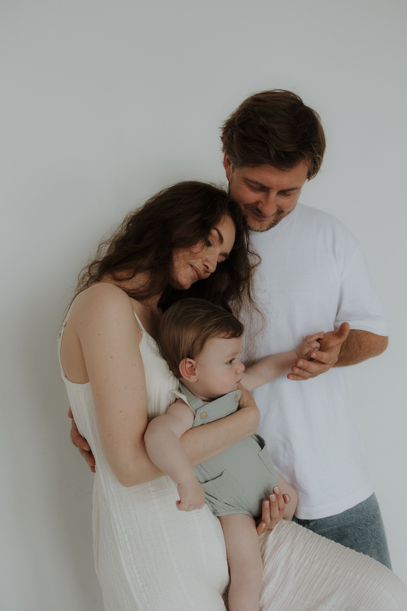 Happy family with parents and baby posing together against a white background.