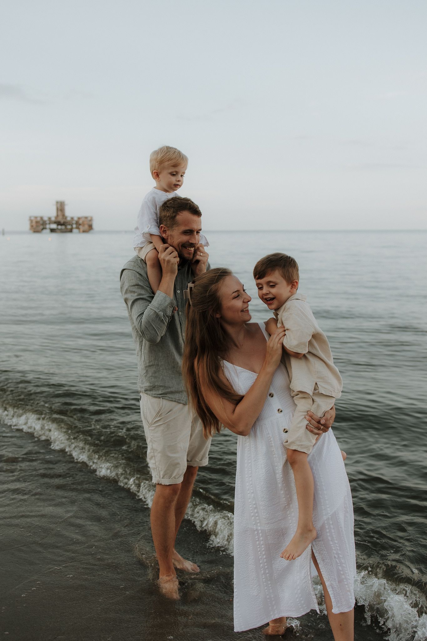 Happy family of four playing in ocean waves at sunset on a sandy beach.