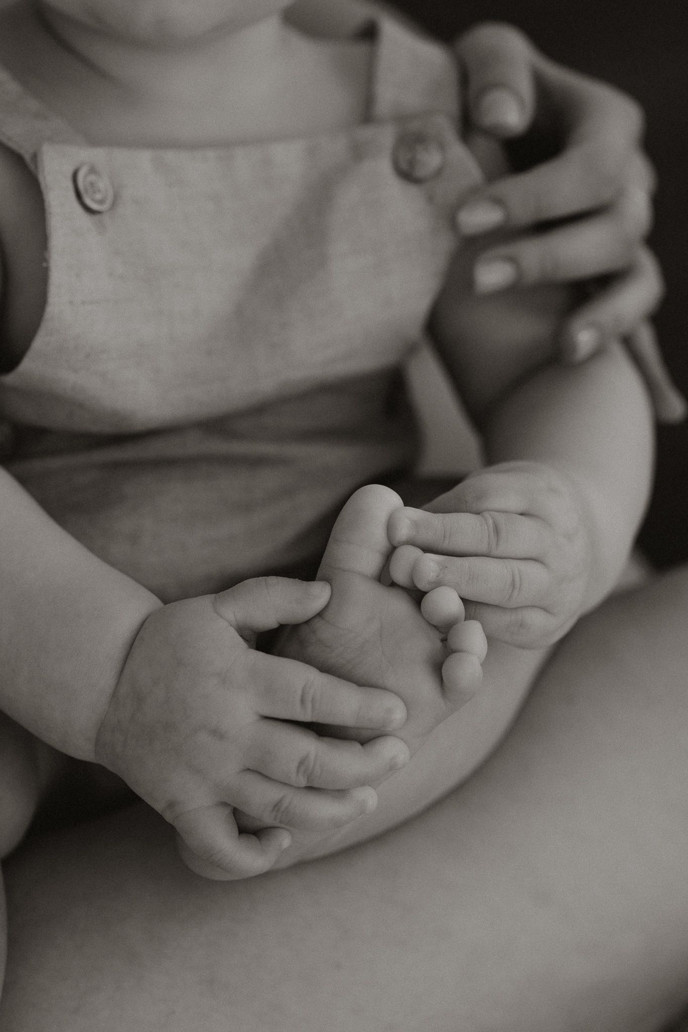 Black and white close-up of a baby's tiny feet and hands held by a parent.