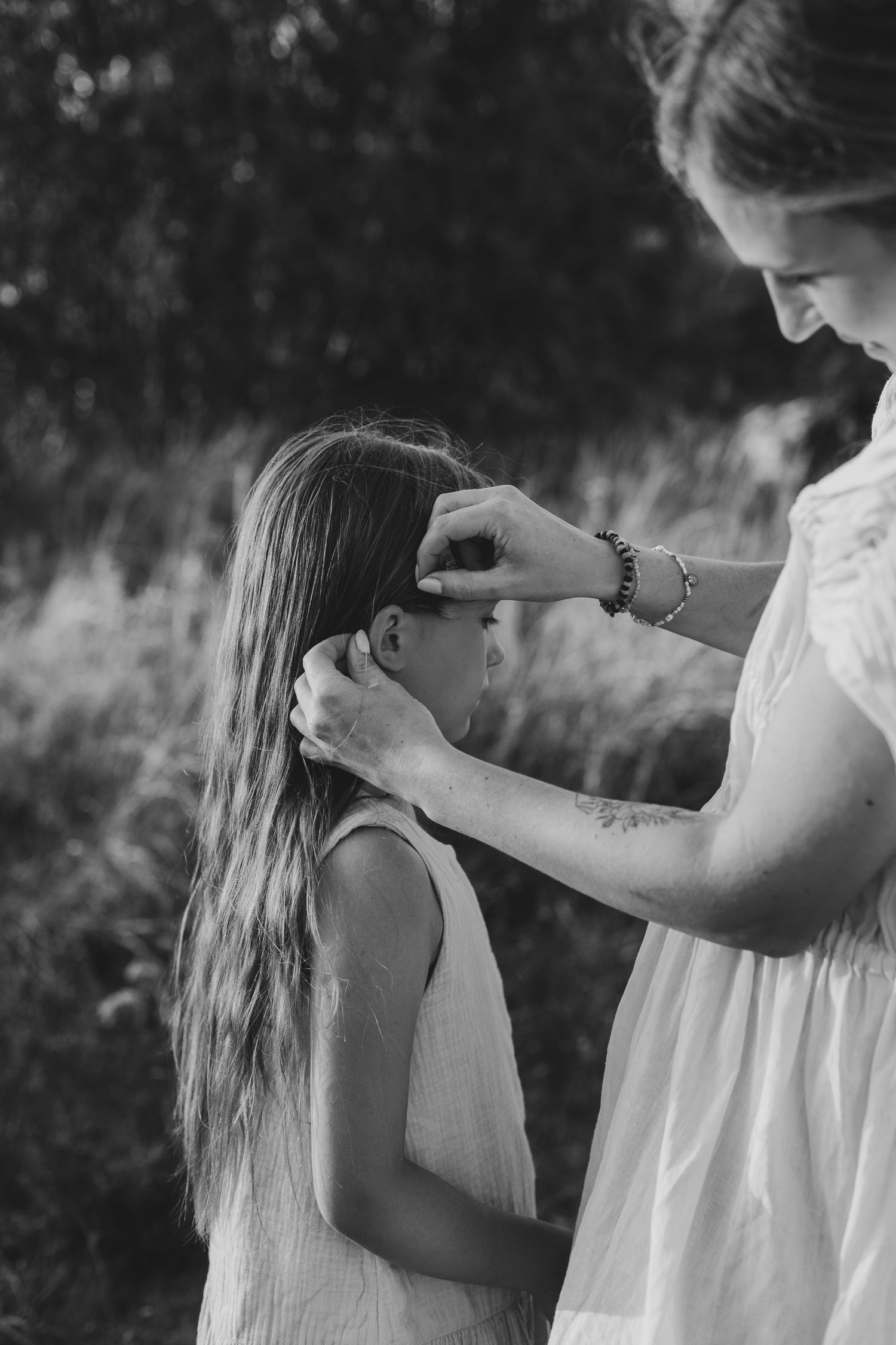 Black and white image of a mother gently styling her daughter's long hair outside.