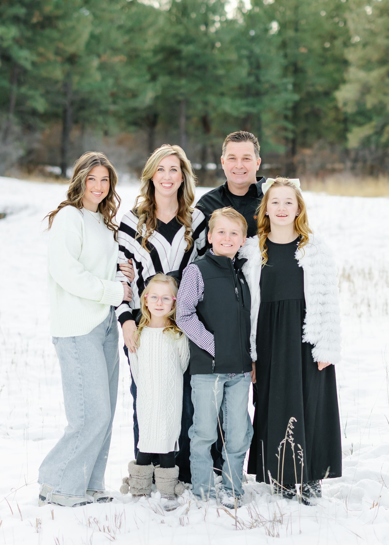 A family portrait captured in a snow-covered field with pine trees in the distance.
