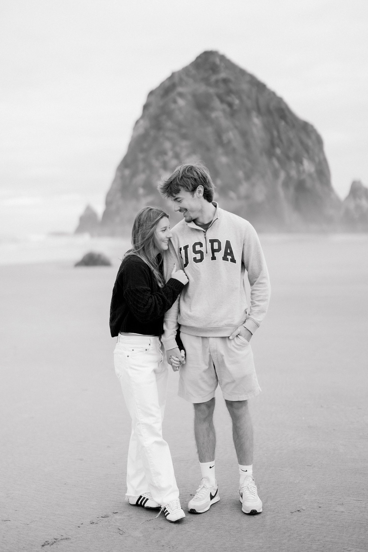 Black and white photo of a couple holding hands on a beach near Haystack Rock.