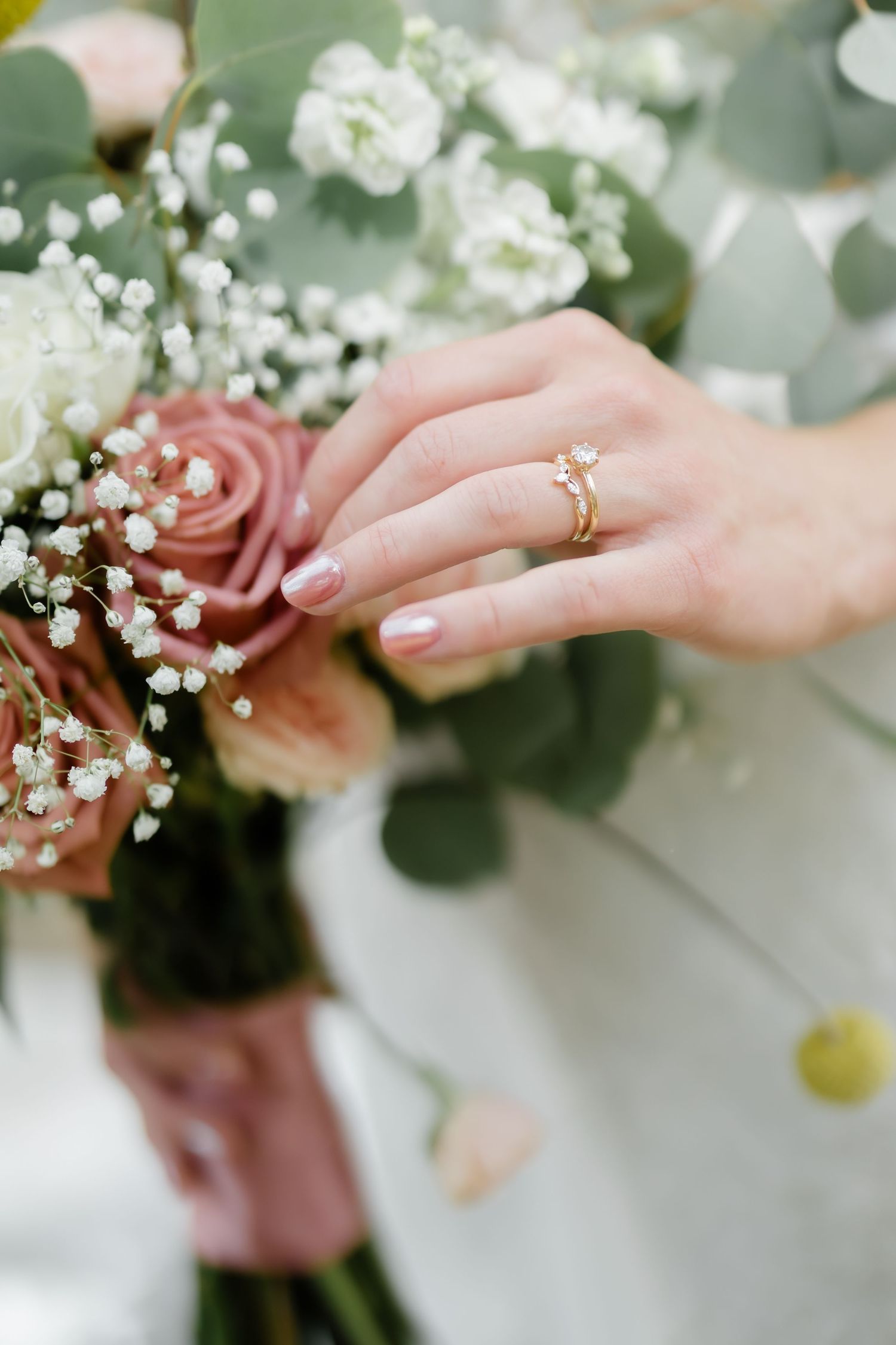 Bride's hand with gold diamond engagement ring resting on a bouquet of pink roses and white baby's breath.
