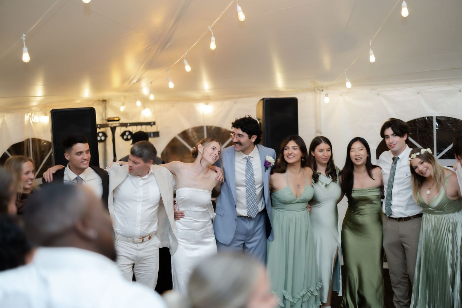 Wedding guests and bridal party smiling together on the dance floor inside a tent reception venue.