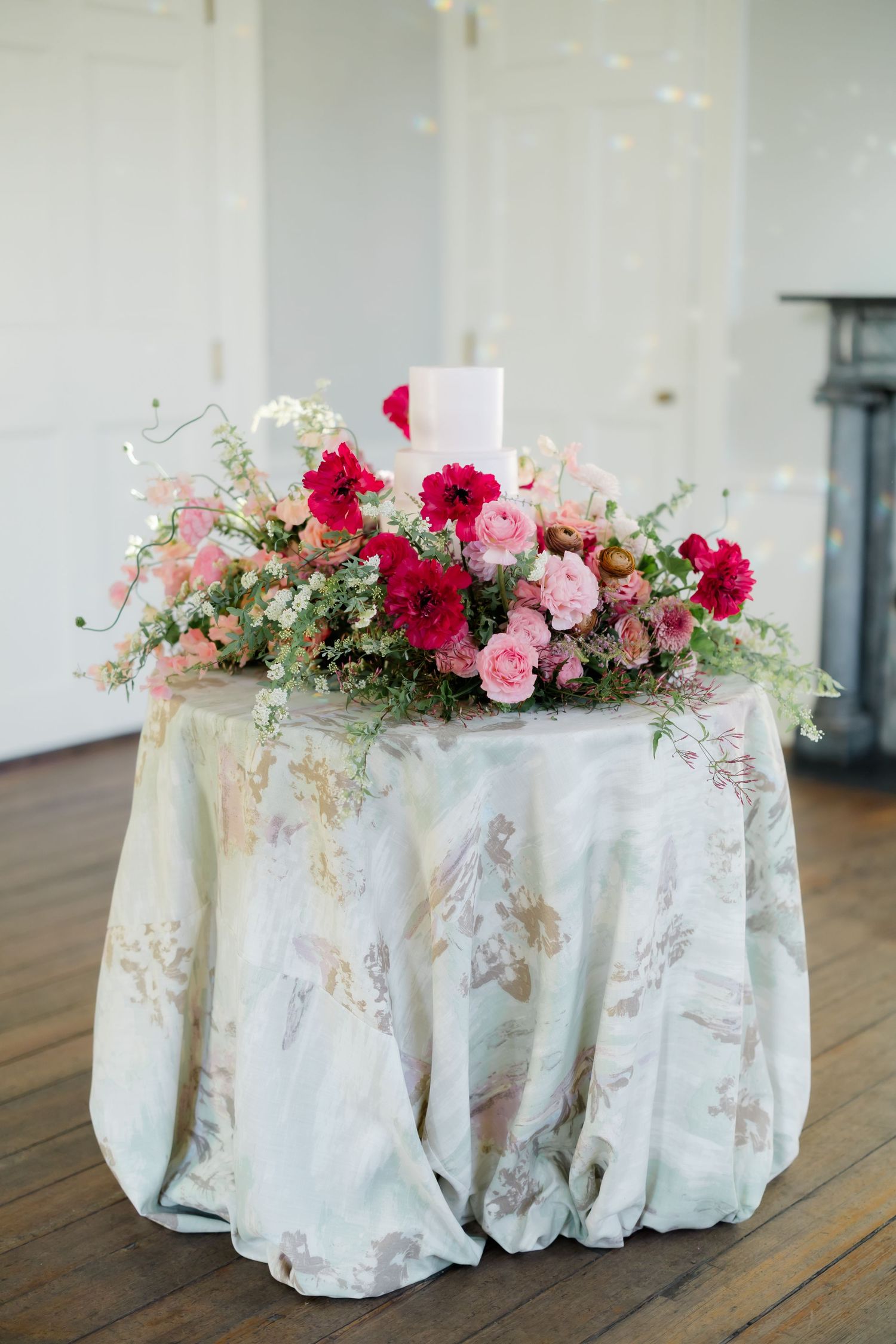 Wedding cake display with vibrant pink and red flowers on an ornate tablecloth.