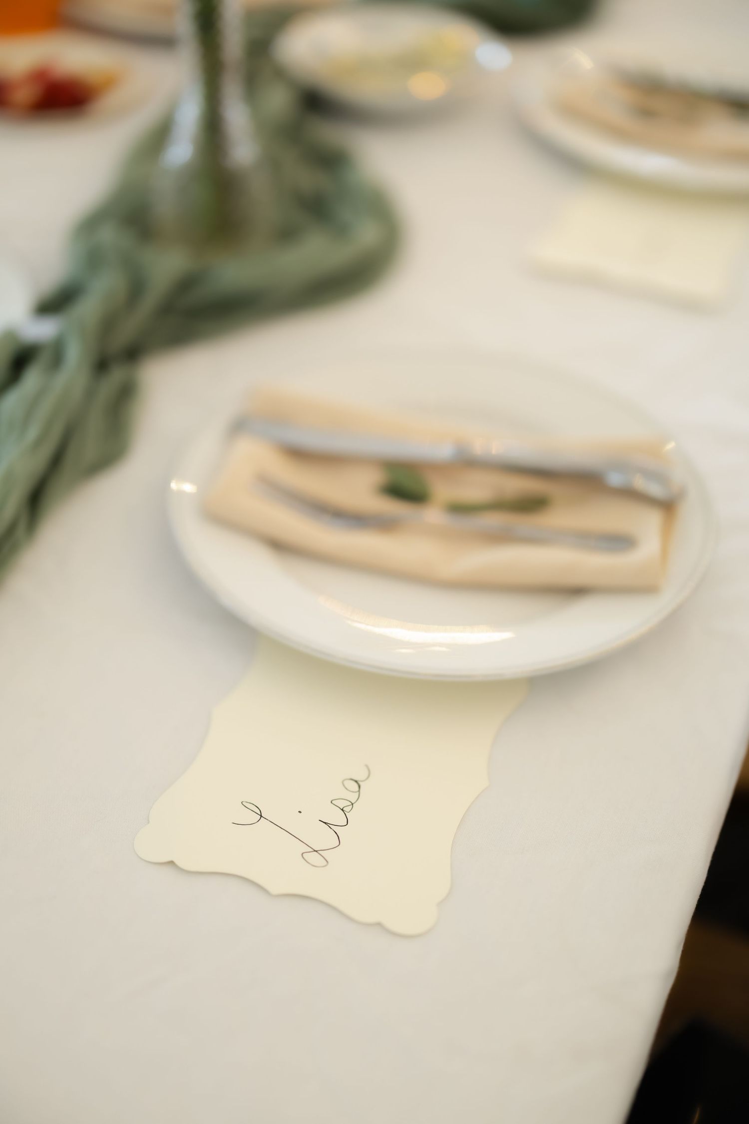 Elegant place setting with a white plate, folded napkin, silverware, and a handwritten name card reading Lisa.