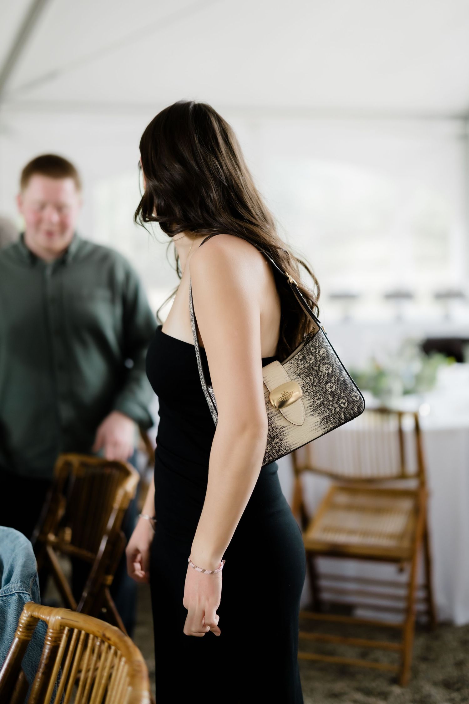 Elegant woman in black dress carries ornate clutch purse at indoor wedding reception.