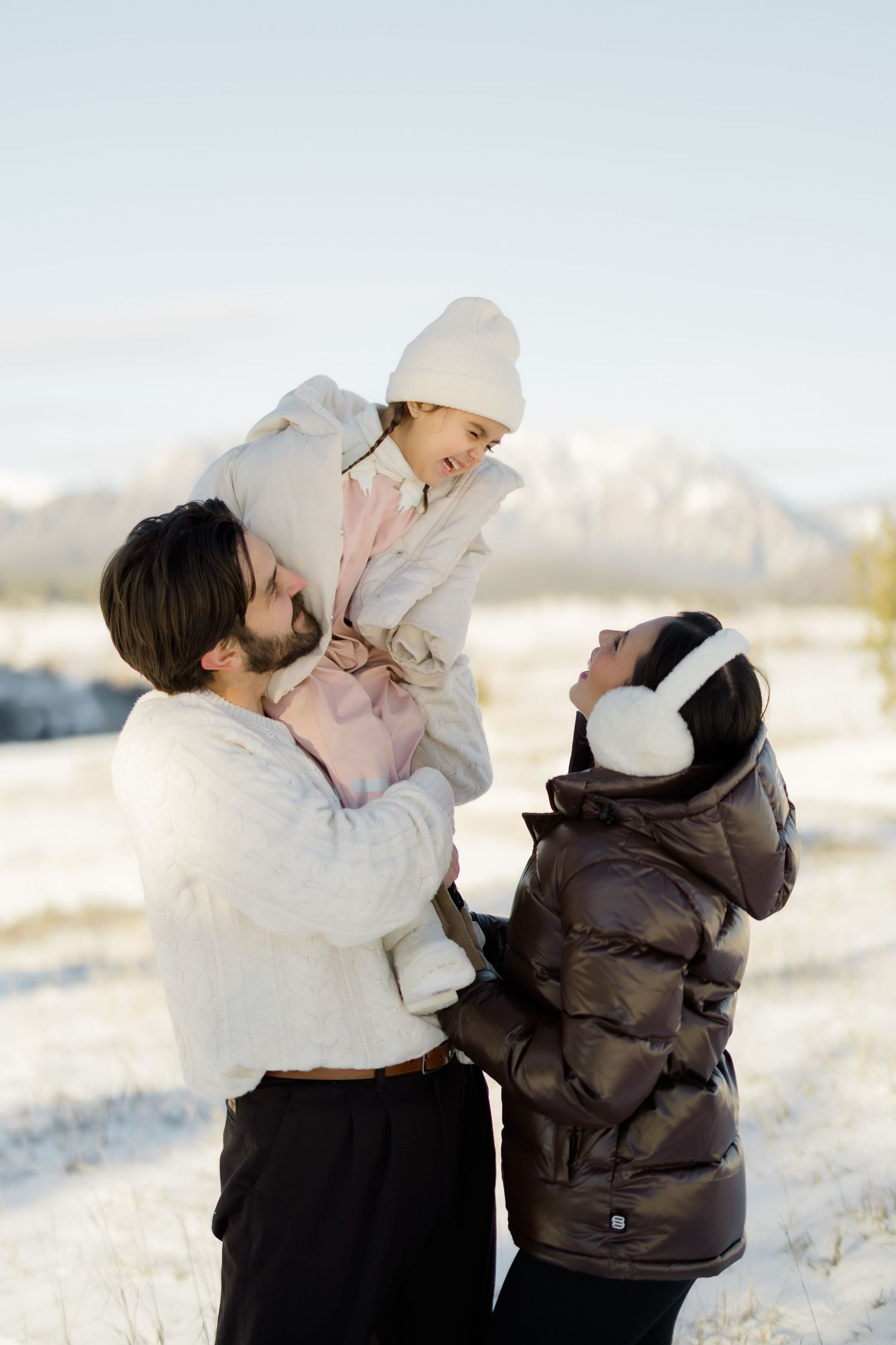 Family sharing intimate moments in snowy mountain setting wearing winter coats.