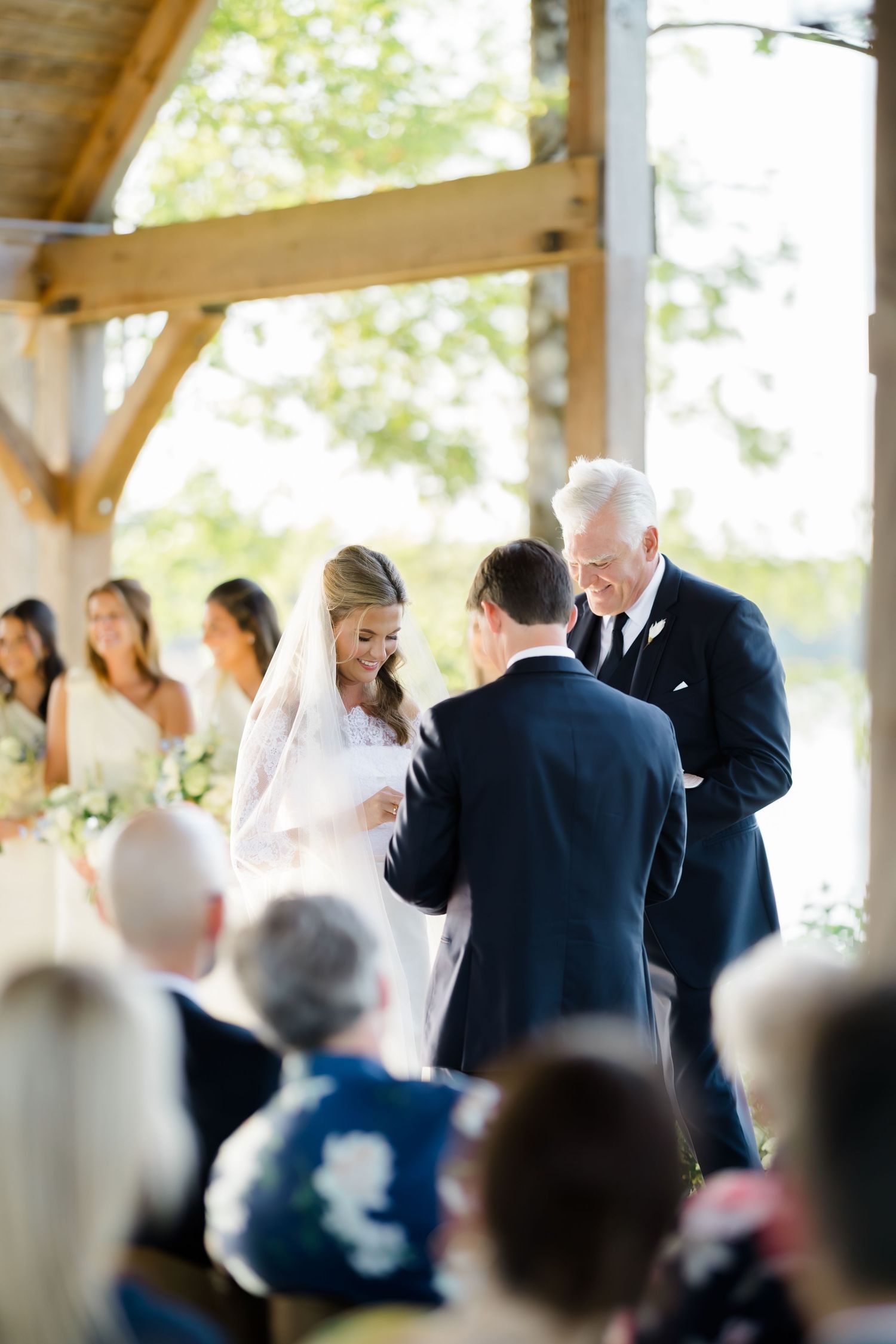 Bride and groom exchange vows during an outdoor barn wedding ceremony with bridesmaids and guests looking on.