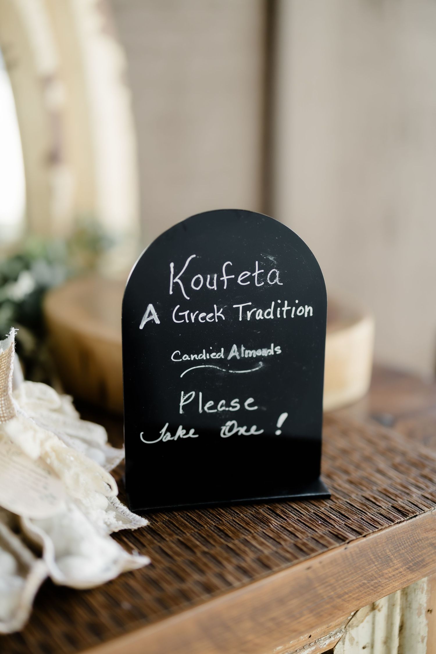 A black chalkboard sign explaining Koufeta, a Greek tradition of candied almonds, inviting guests to take one at a wedding.