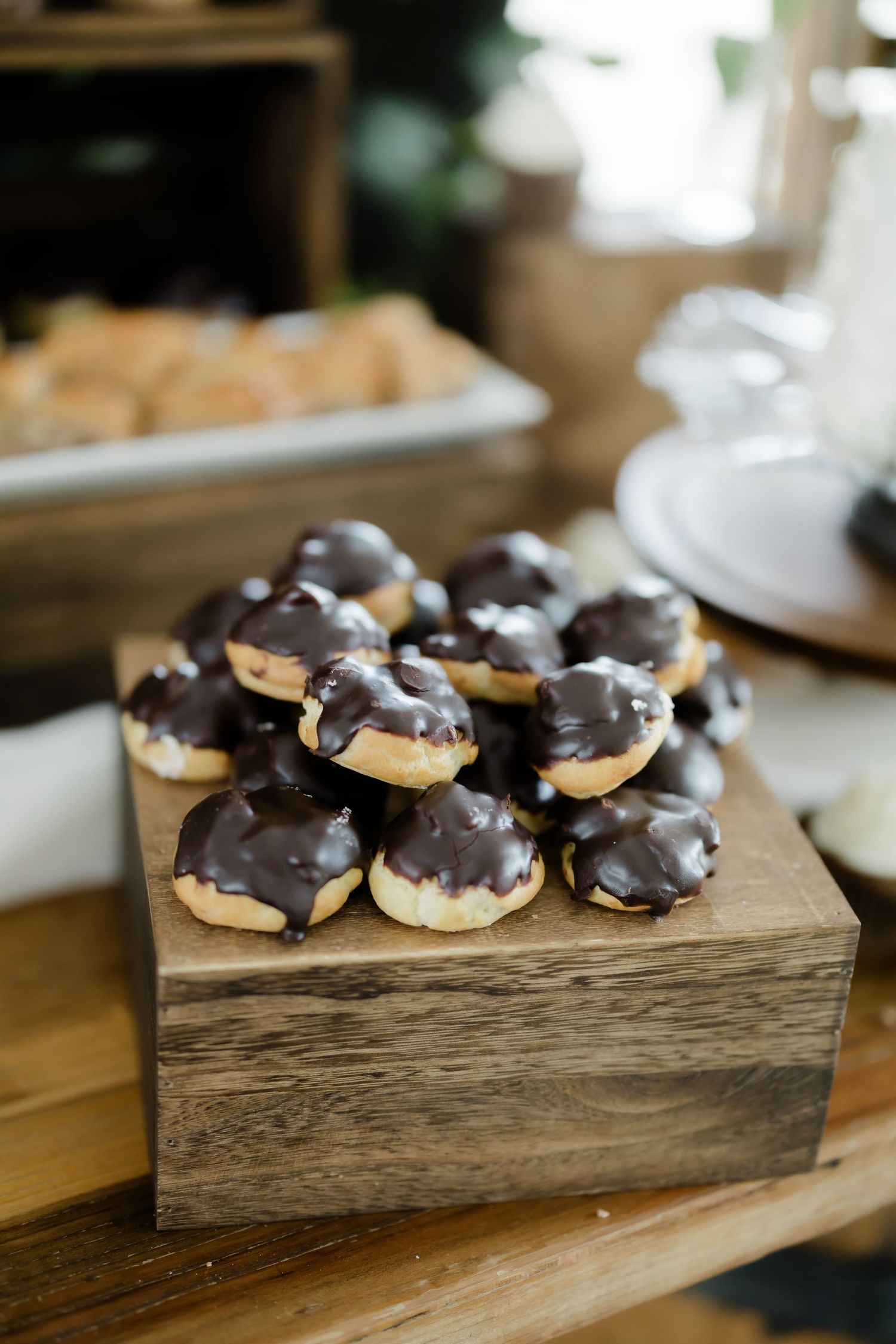 Chocolate glazed cream puff pastries stacked on rustic wooden display at wedding dessert table.