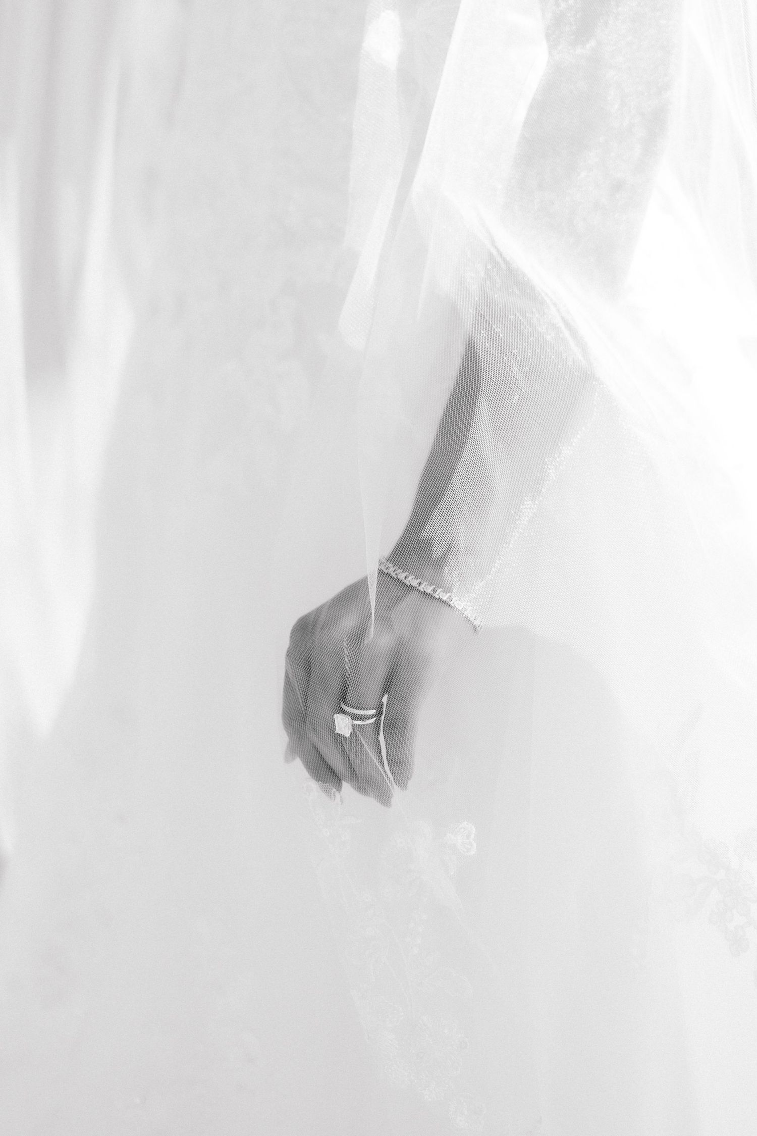 Black and white photo of a bride's hand wearing a ring and bracelet against a white wedding dress.