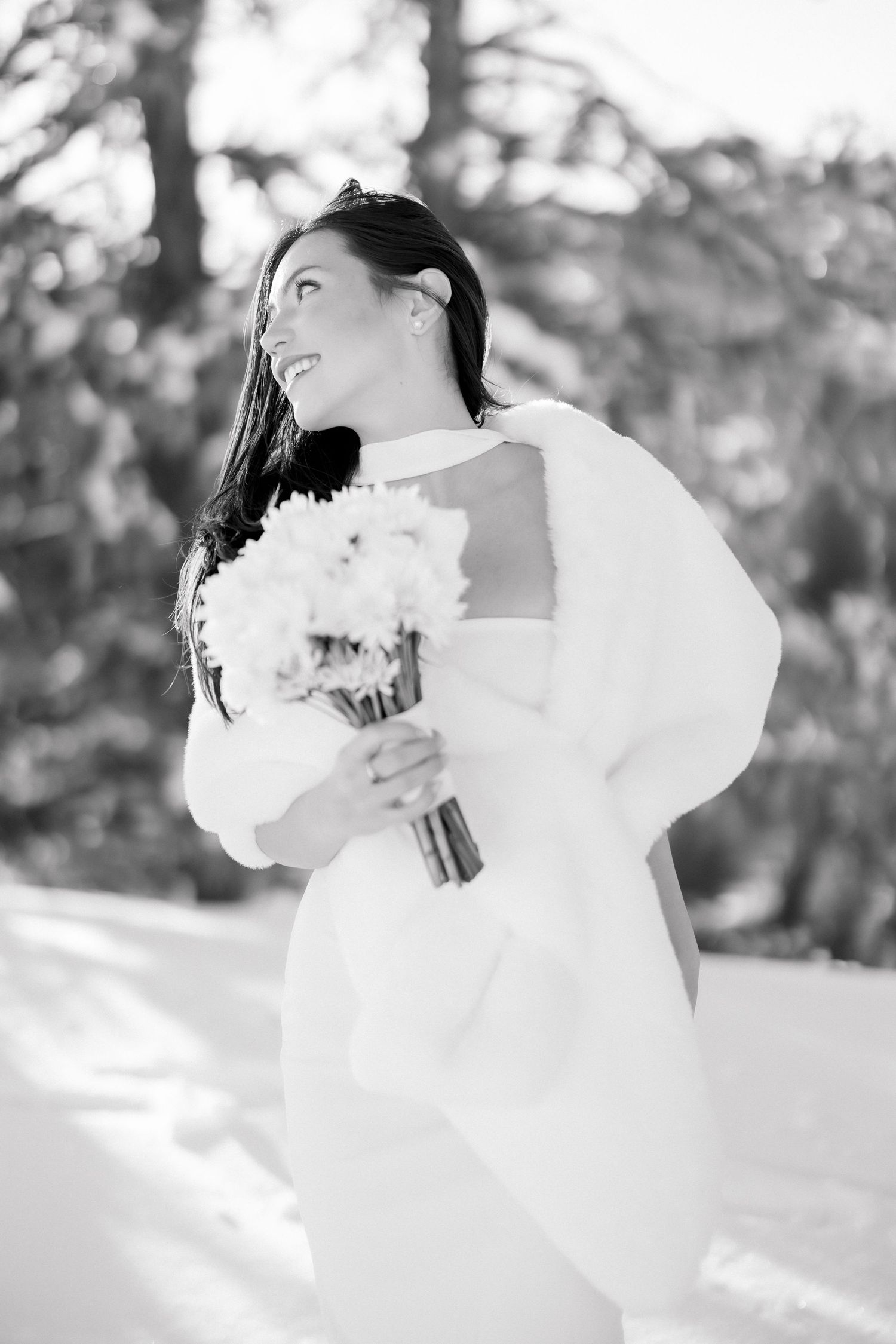 Black and white portrait of smiling bride in fur wrap holding white bouquet in winter setting.