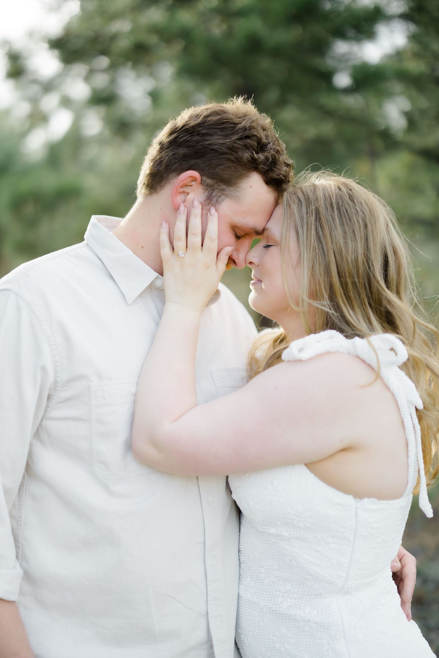 Couple sharing an intimate forehead touch moment outdoors with soft natural lighting among pine trees.