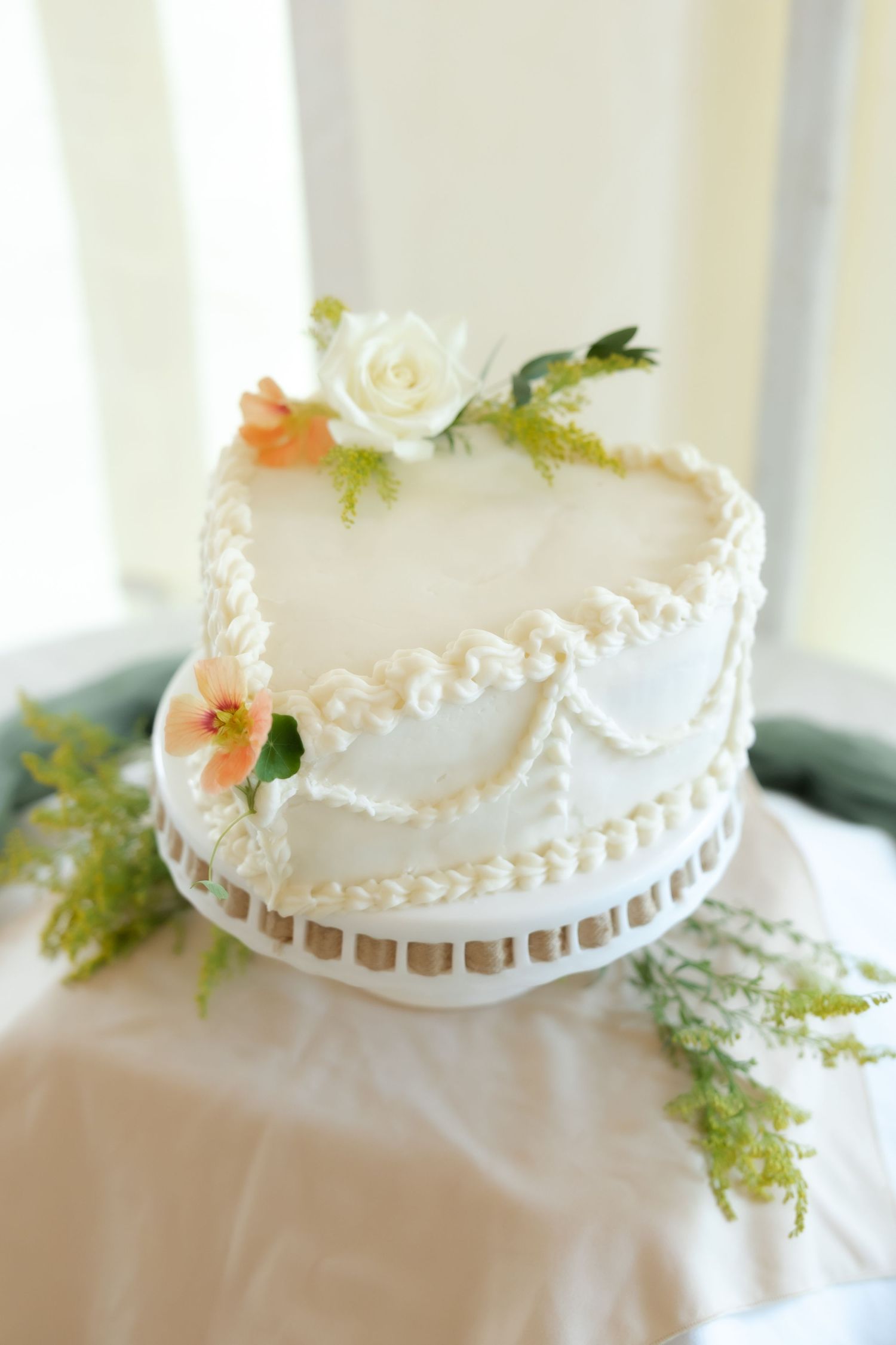 Elegant single-tier white wedding cake with pearl piping, peach flowers, and a white rose on a decorative cake stand.