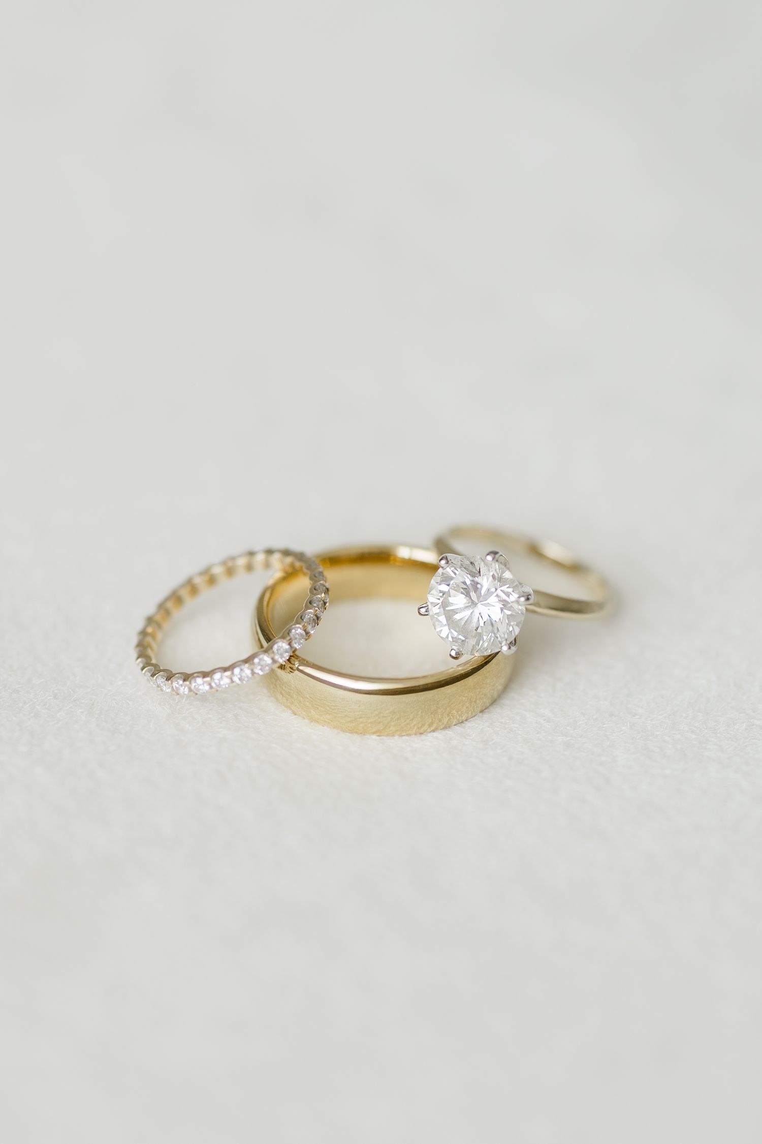 Close up view of delicate gold wedding rings with diamonds on white suede surface.