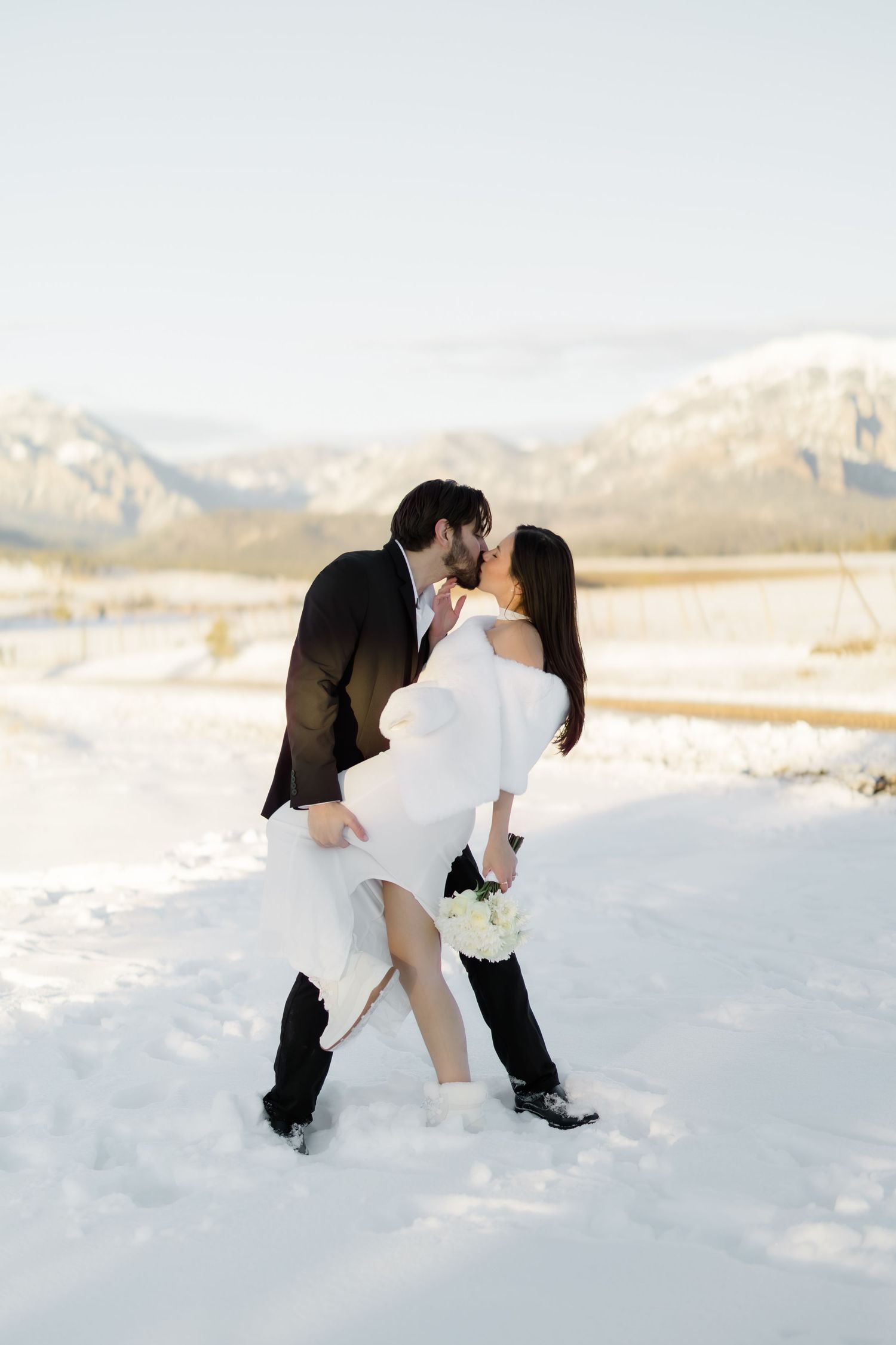 Bride and groom share a passionate kiss in a snowy winter wedding setting.