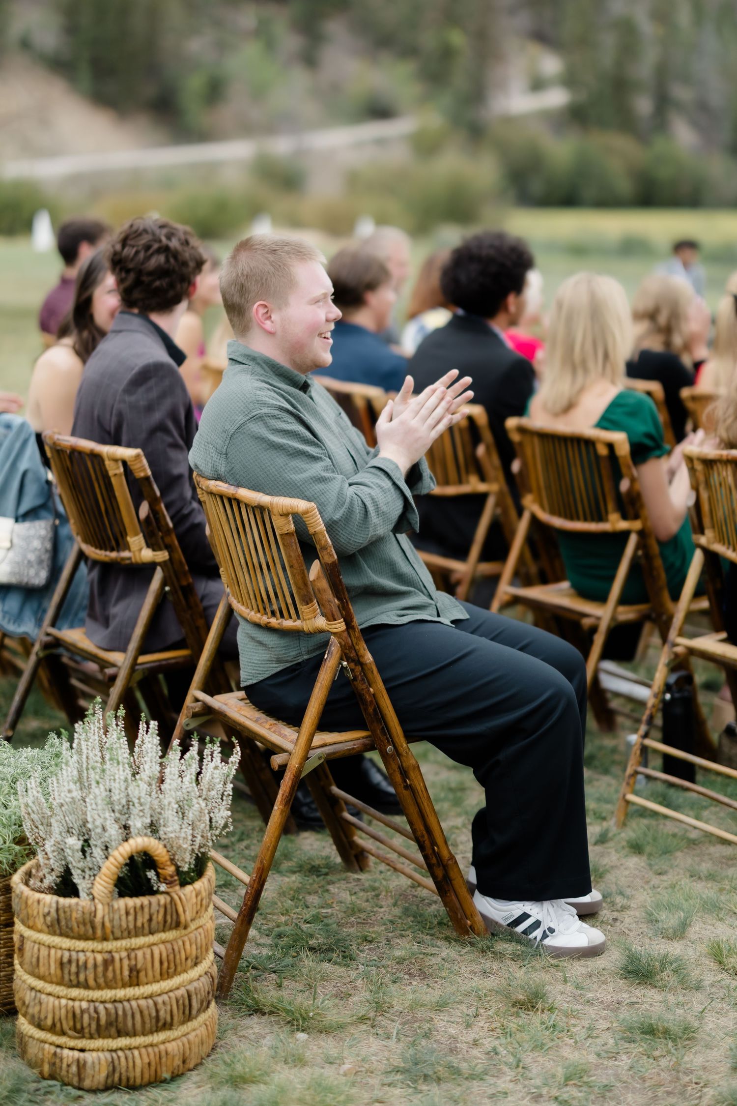 Smiling guest clapping at outdoor mountain wedding ceremony seated on wooden folding chairs.