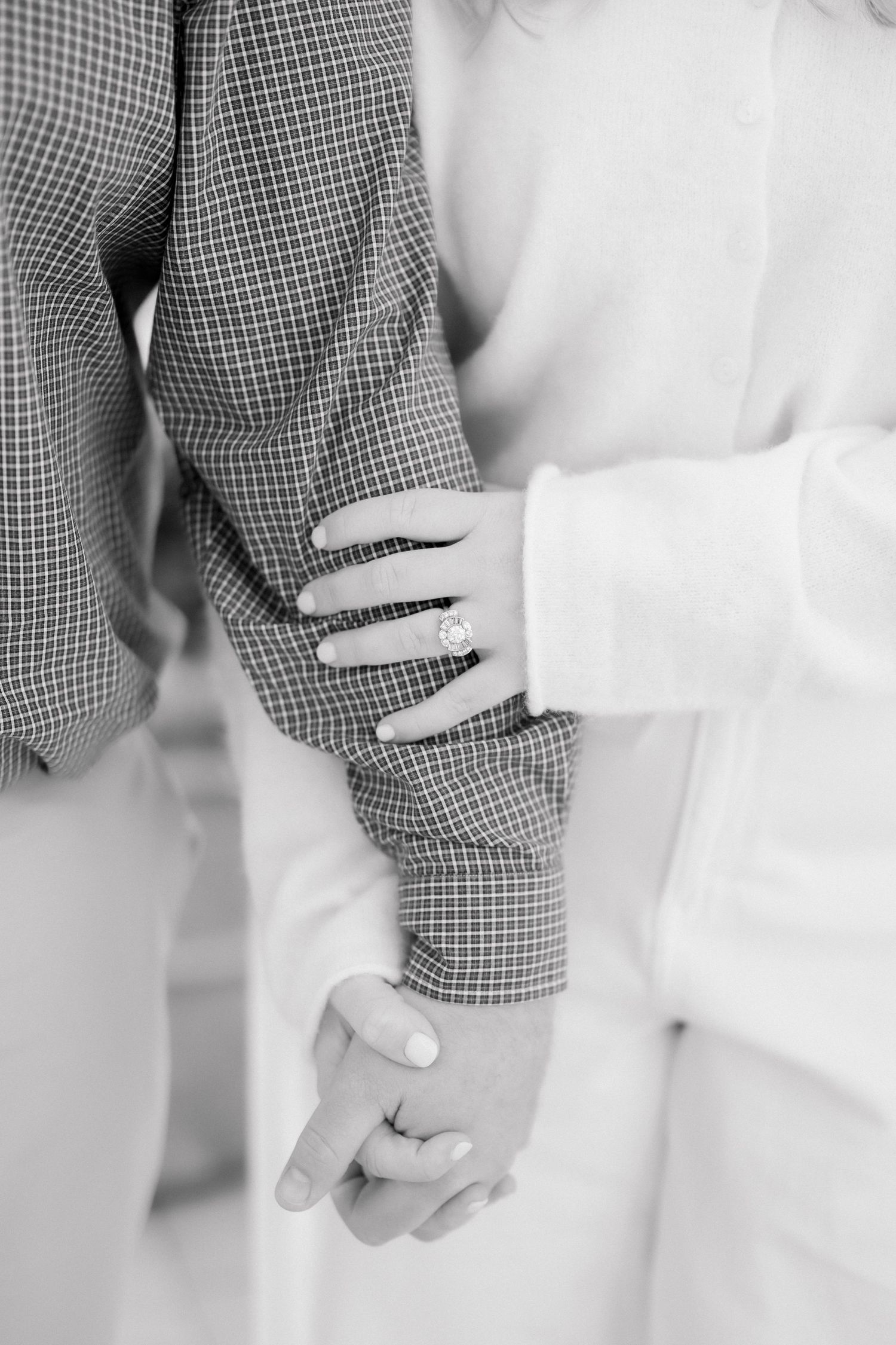 Black and white photo of a couple holding hands, woman wearing an engagement ring, romantic moment captured.