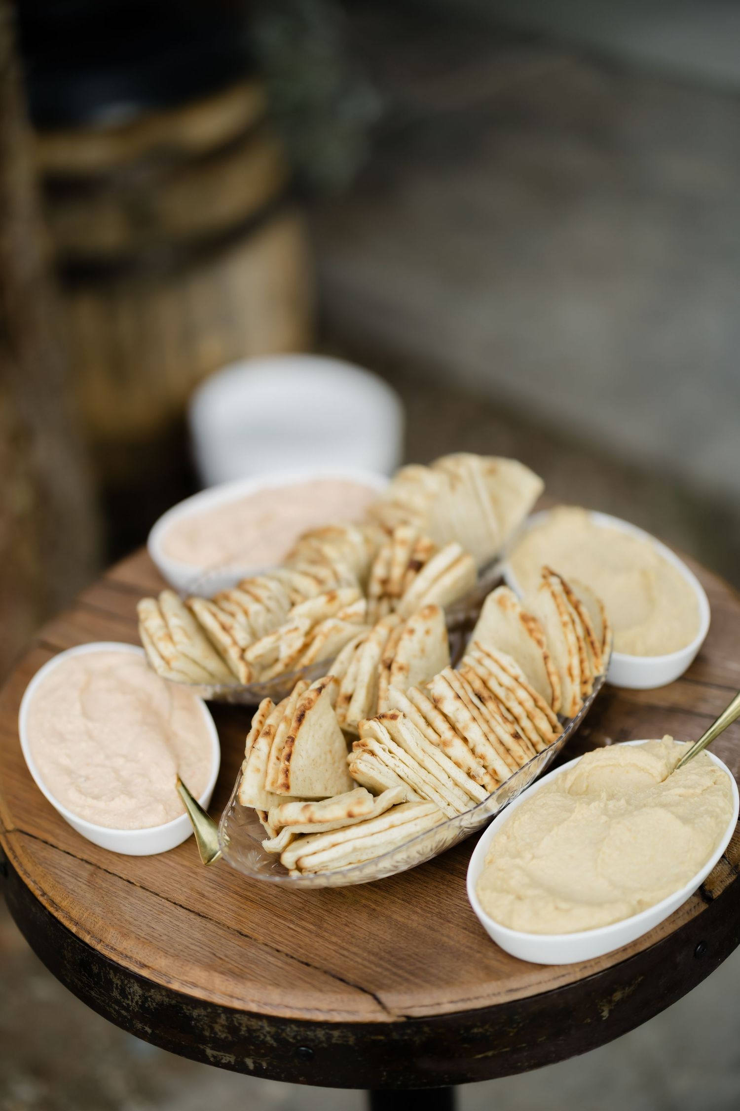 Grilled pita bread slices arranged on a wooden table with bowls of hummus and creamy dips.