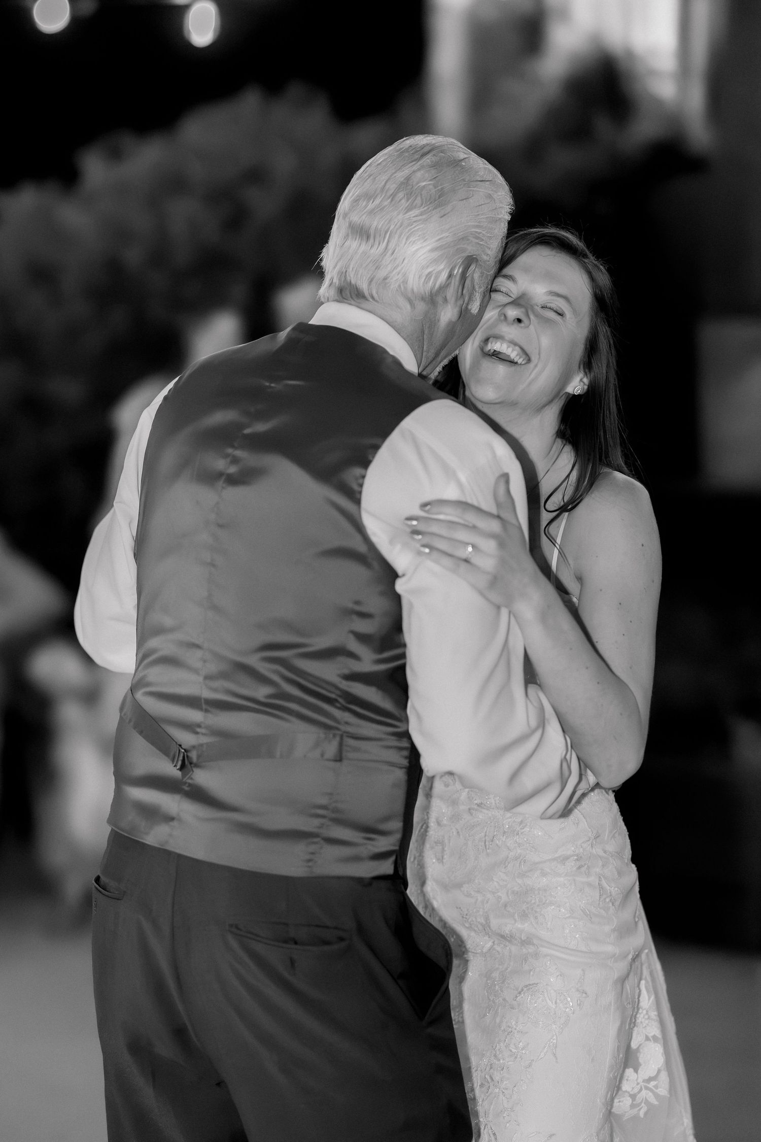 Black and white photo of a bride laughing joyfully while sharing a dance with an older man at a wedding reception.
