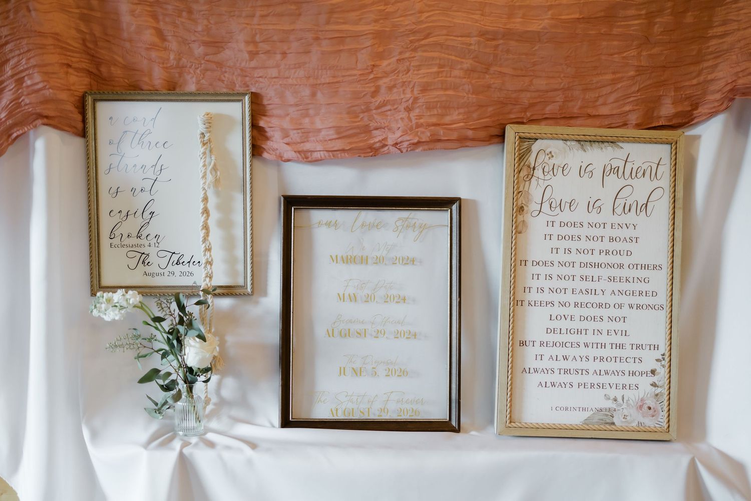 Three gold-framed wedding signs with calligraphy script displayed on white linen table with floral decor.