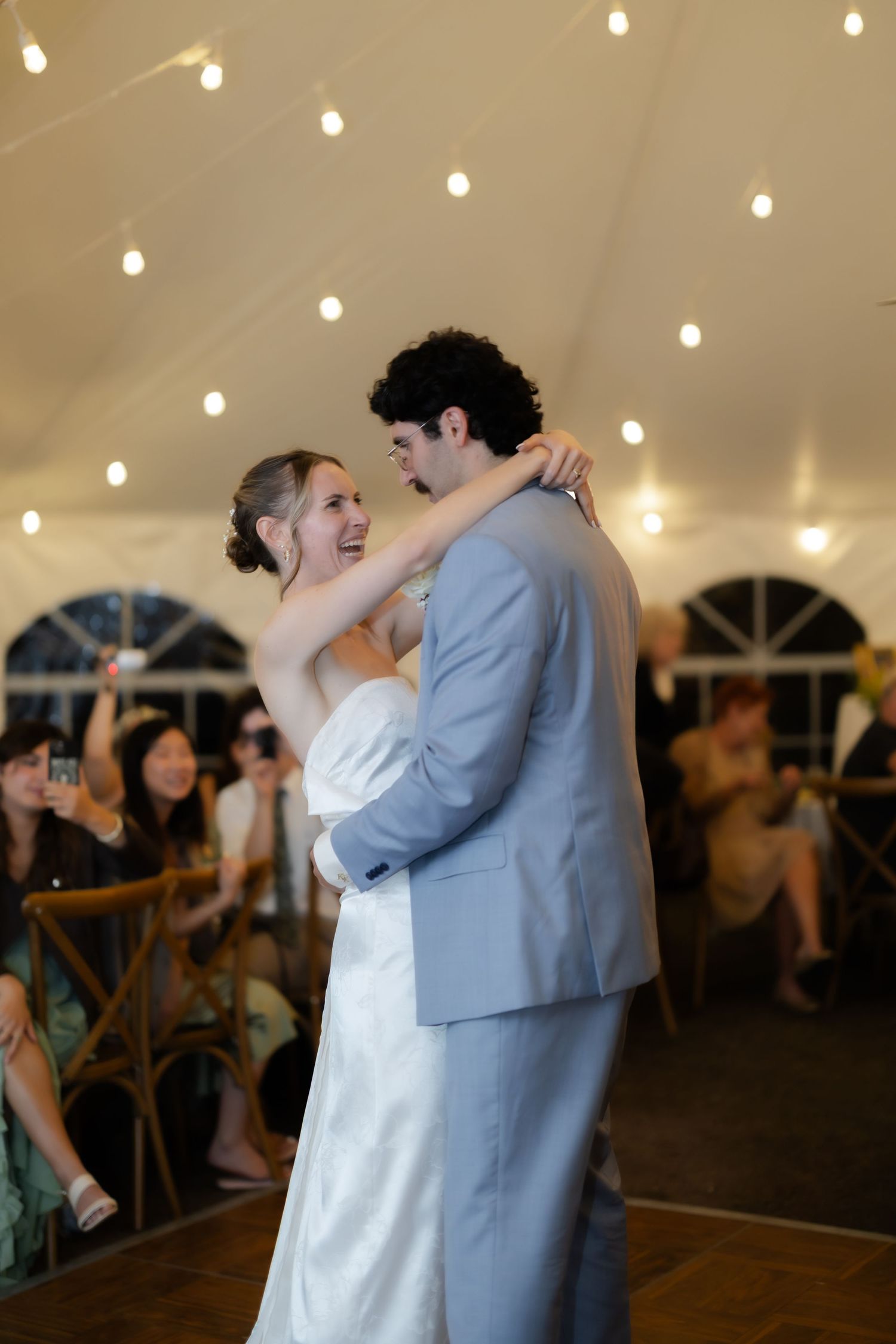 Bride and groom share their first dance under string lights in a elegant white wedding tent.