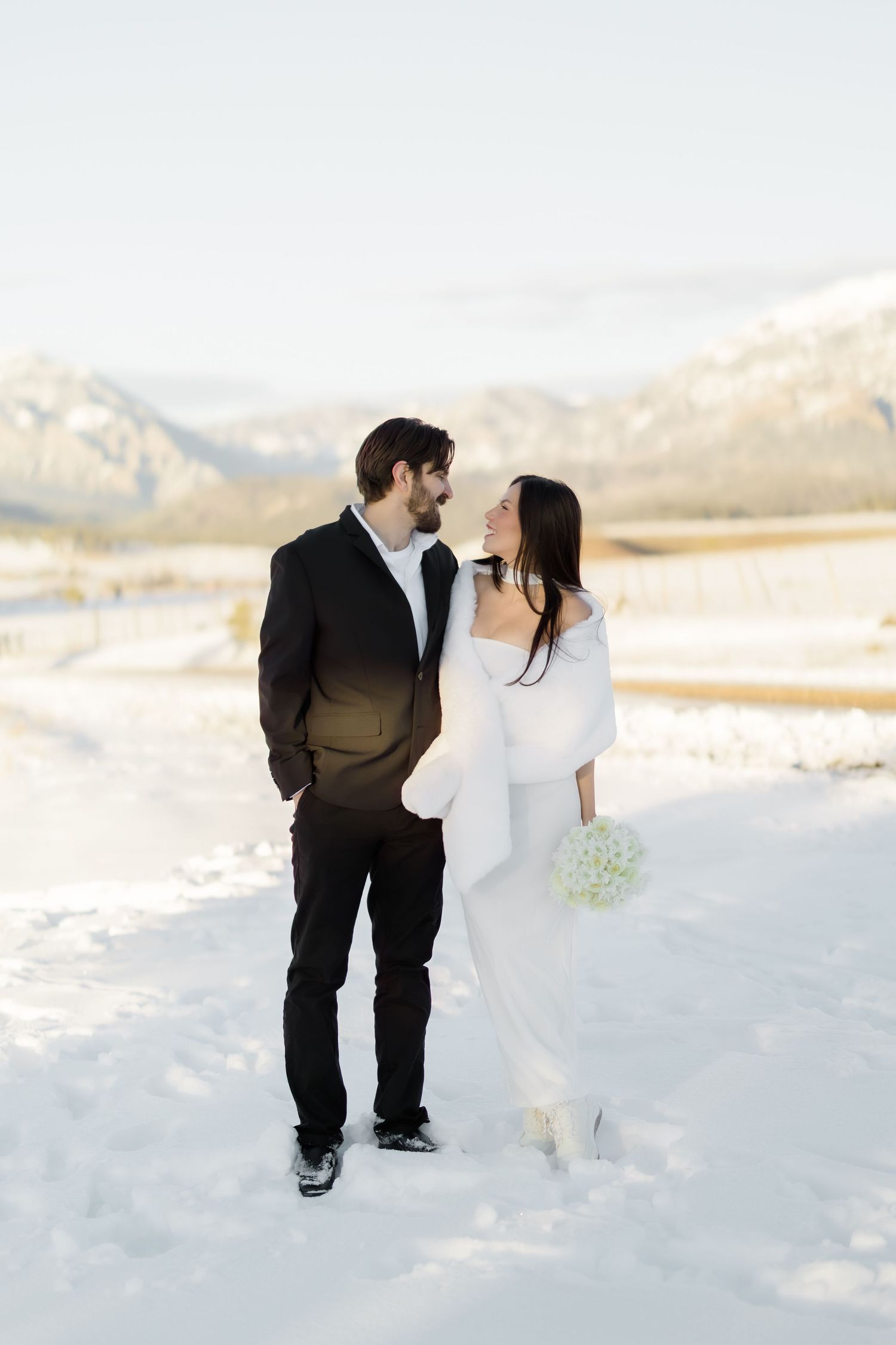 Bride and groom walking together in wedding attire across a snowy landscape with the San Juan mountains in the background.