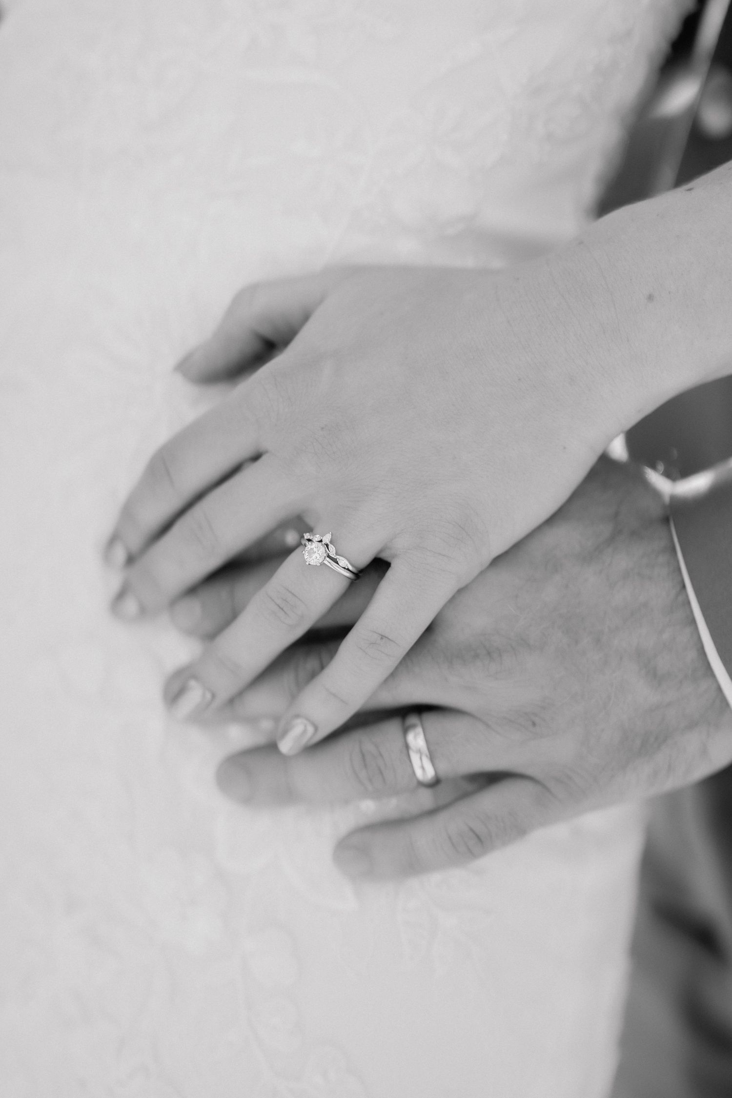Black and white photo of newlyweds hands together showing diamond engagement ring and wedding band.