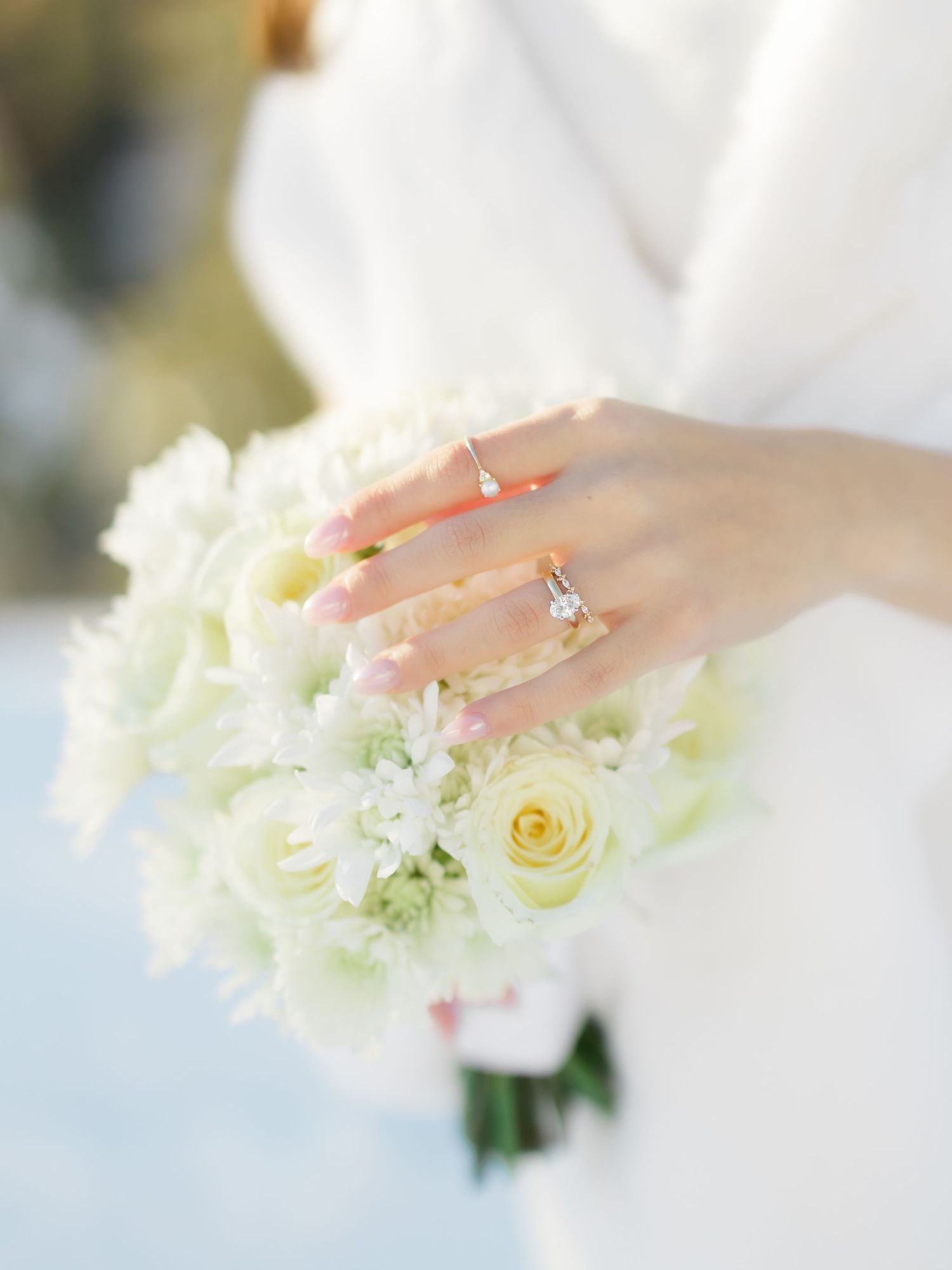 Bride holding white floral bouquet with roses displaying elegant diamond engagement ring on her finger.
